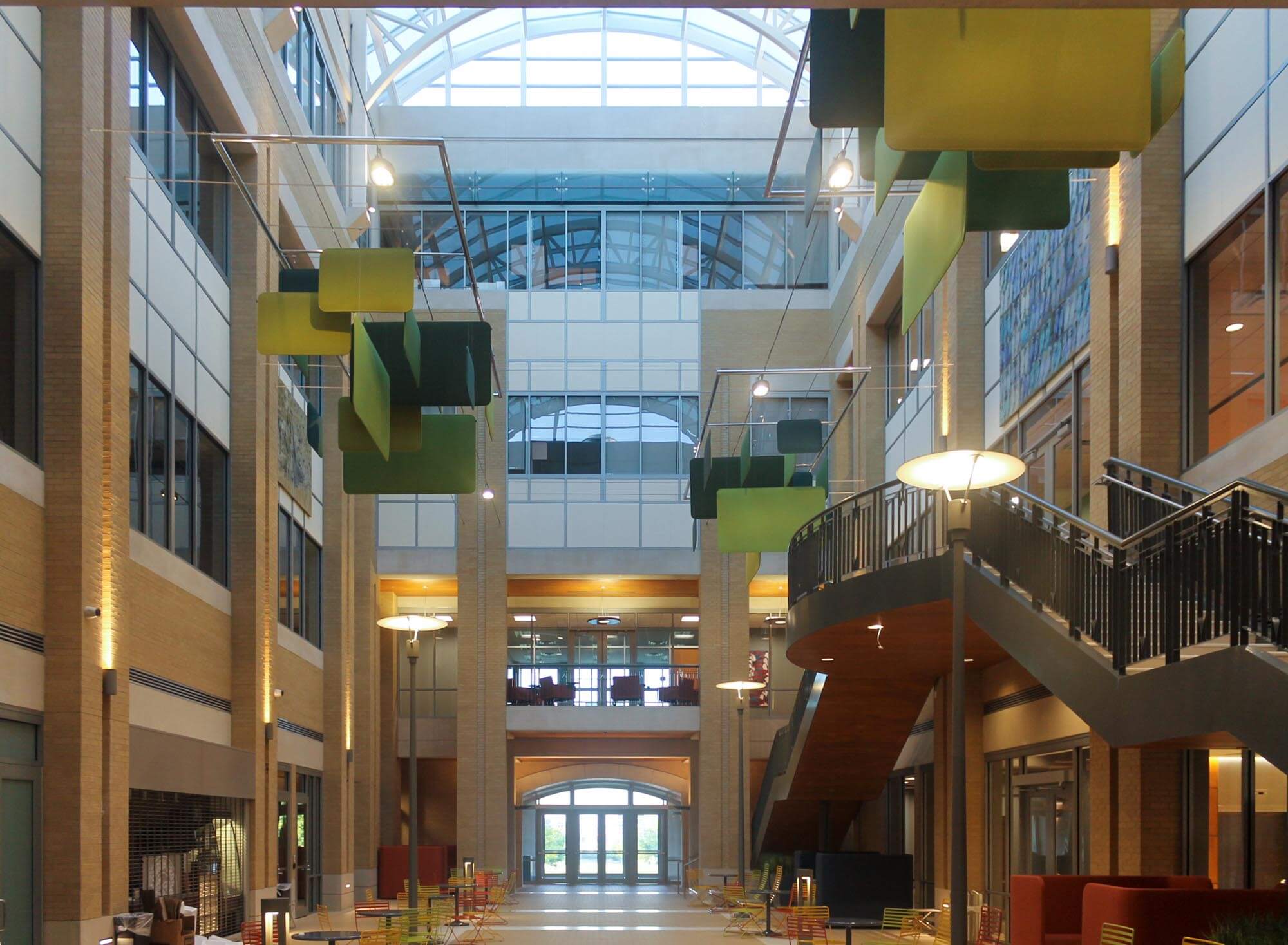 Central atrium featuring hanging green geometric sculptures, curved staircases and skylight