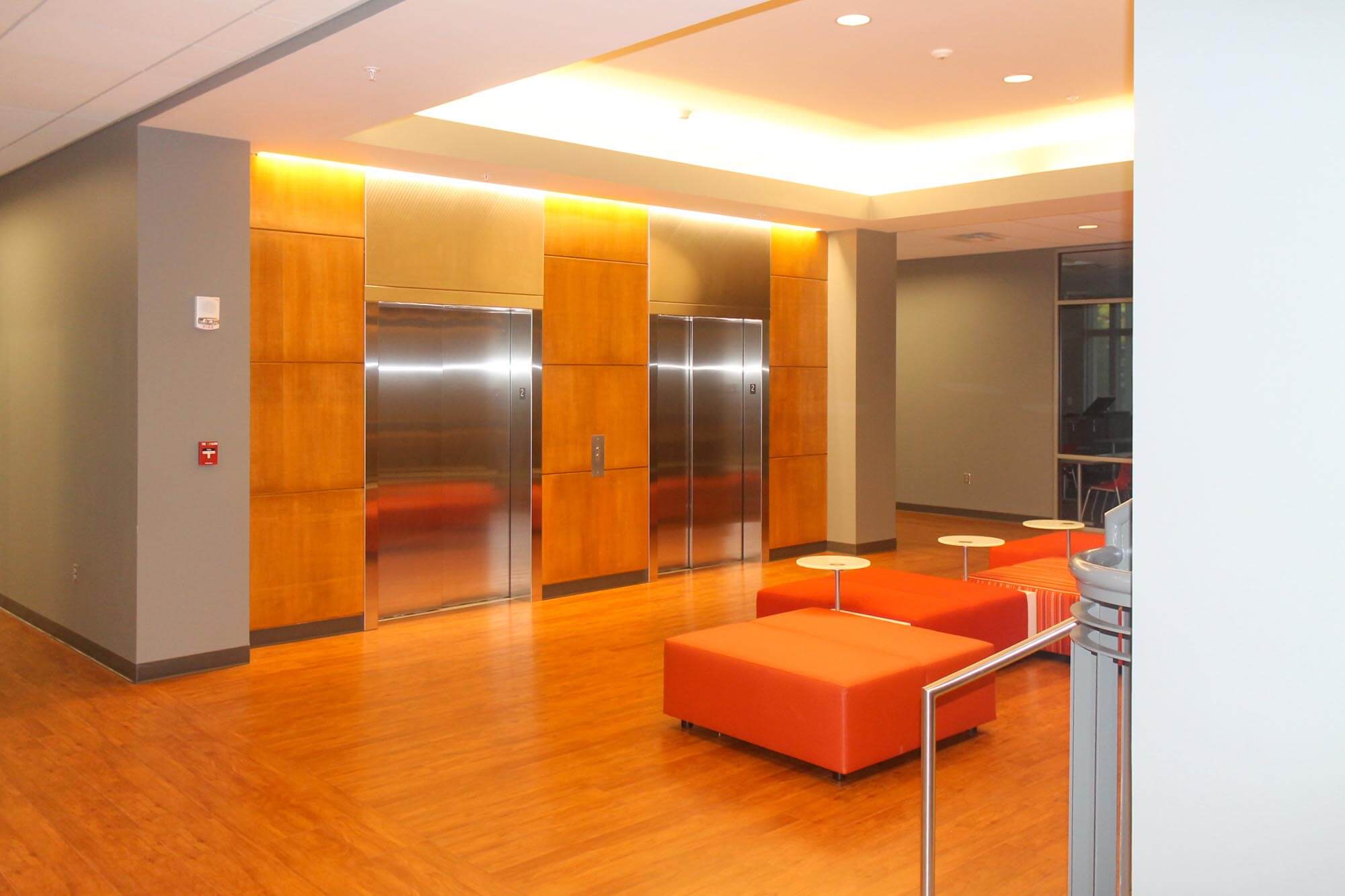 Lobby area with stainless elevators set into a wood-paneled wall and orange modular seating