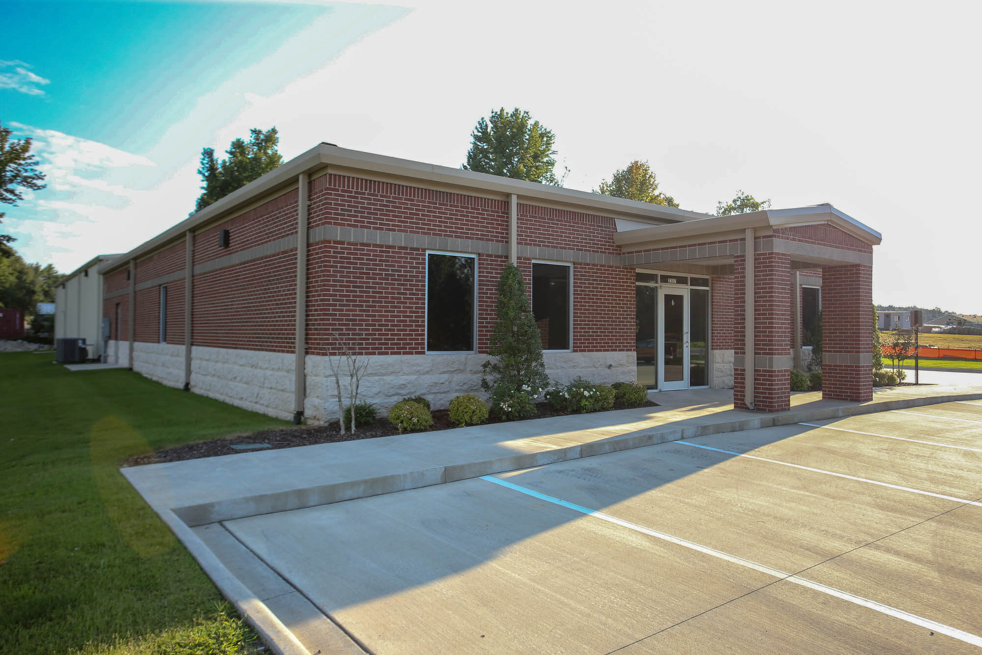 Exterior shot of the Bailey Contractors, Inc. office building taken from an angled perspective, highlighting the red brick and stone façade, covered entrance with metal trim, and large windows
