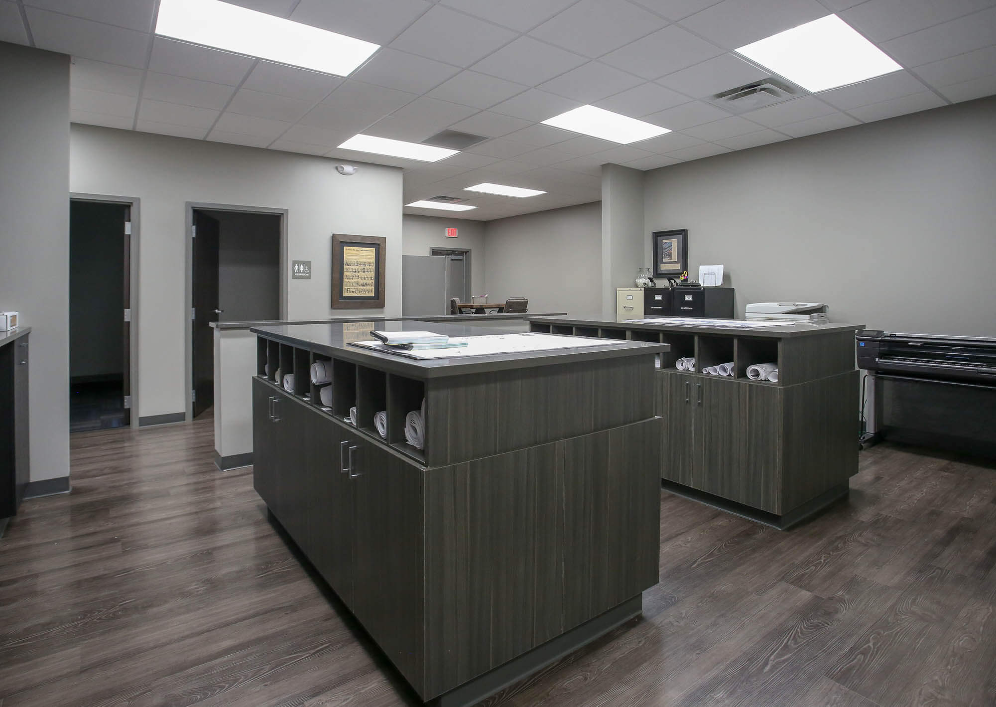 Interior shot of the Bailey Contractors, Inc. office workspace, featuring large dark wood storage islands with built-in cubbies holding rolled-up blueprints