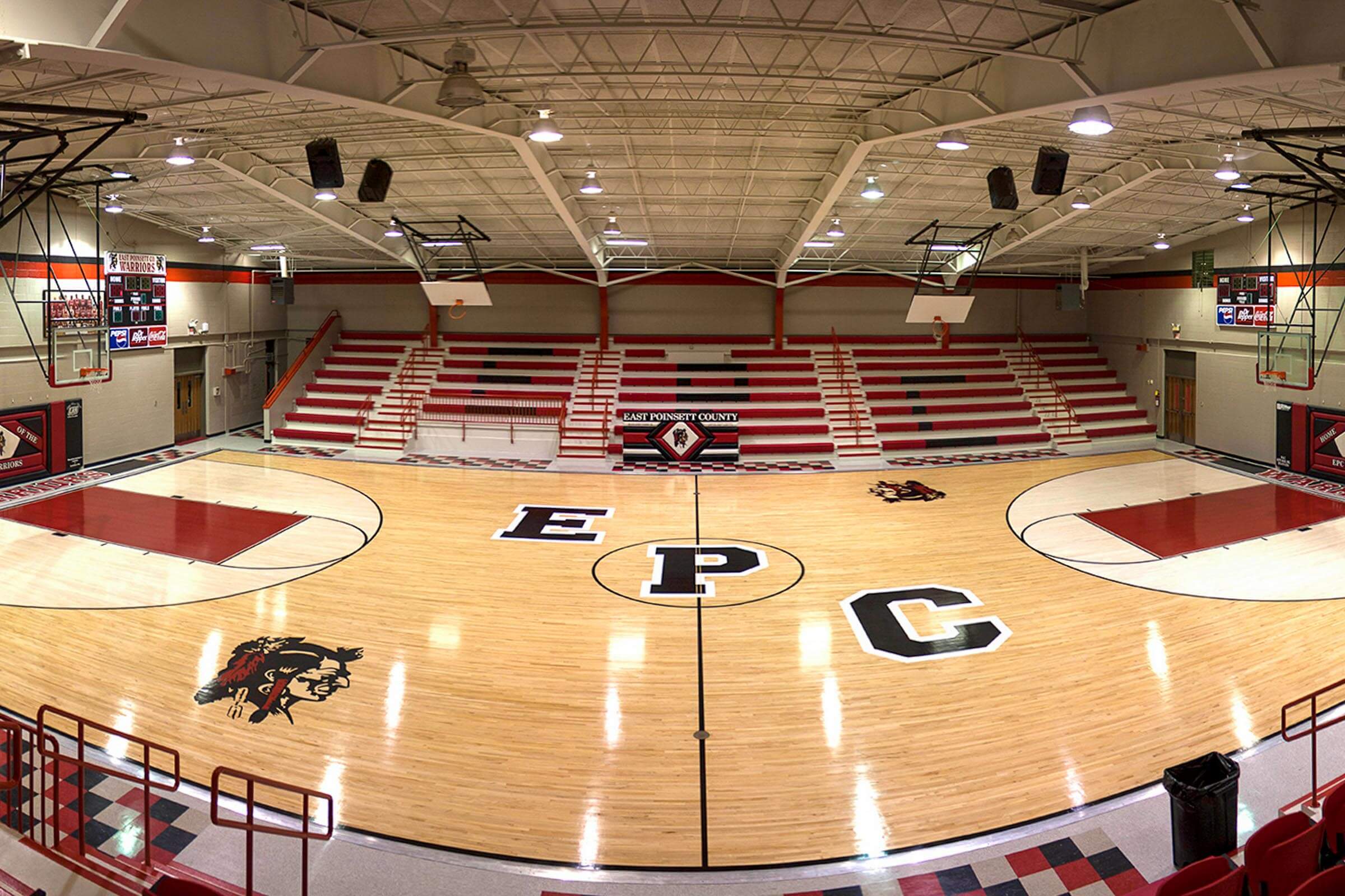 Panoramic view of the renovated gymnasium with polished wooden court featuring large “EPC” letters and warrior mascot, red bleachers and exposed truss ceiling