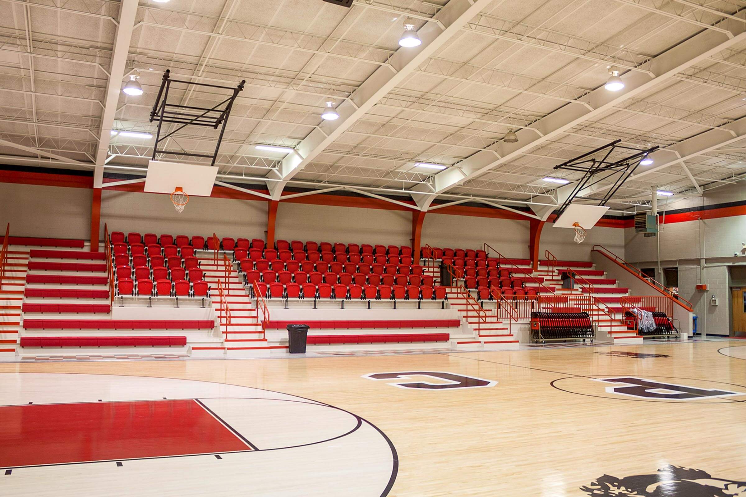 Side view focusing on the red bleacher seating and basketball hoops inside the renovated gymnasium