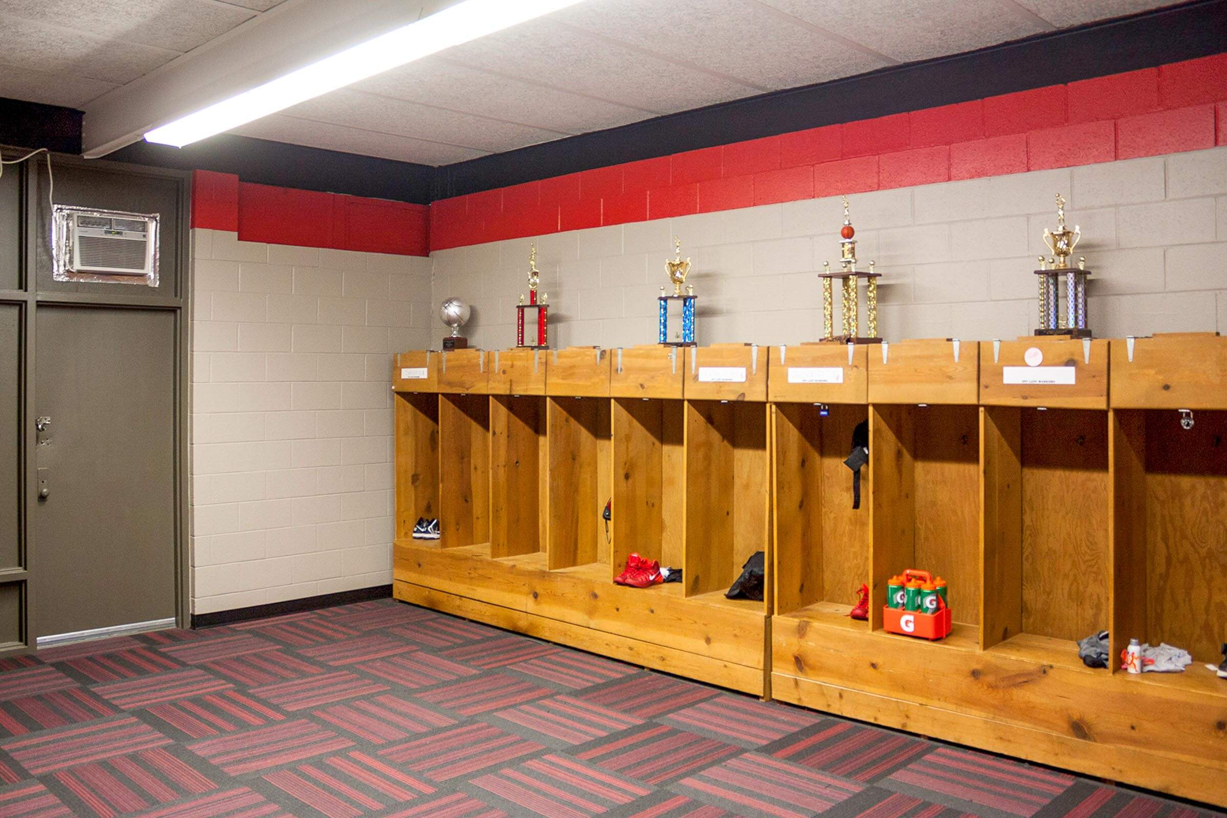 Locker room cubbies with individual compartments, trophies displayed on top and red accent wall