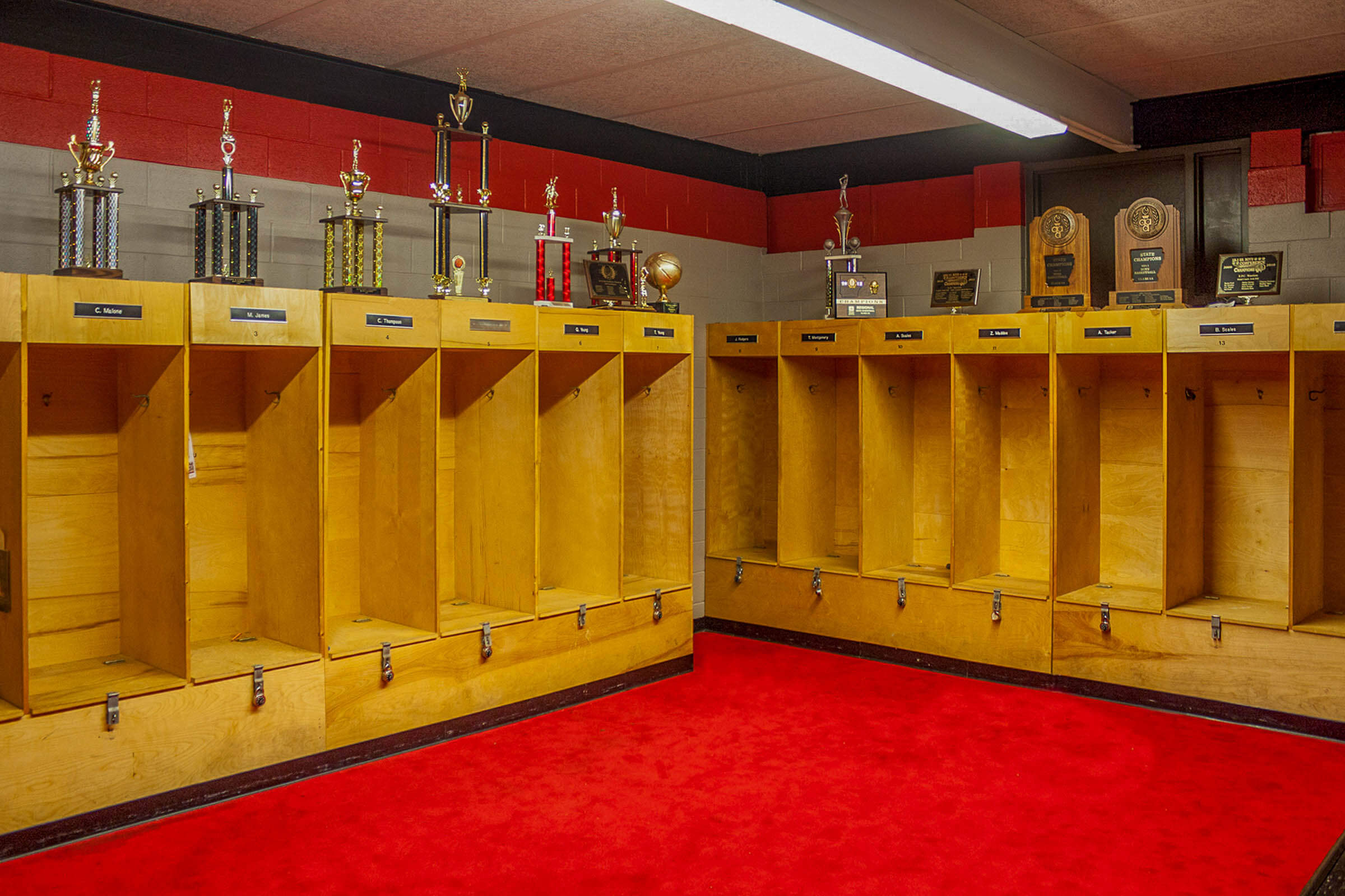 Team locker room with wooden lockers, trophies and bright red carpet