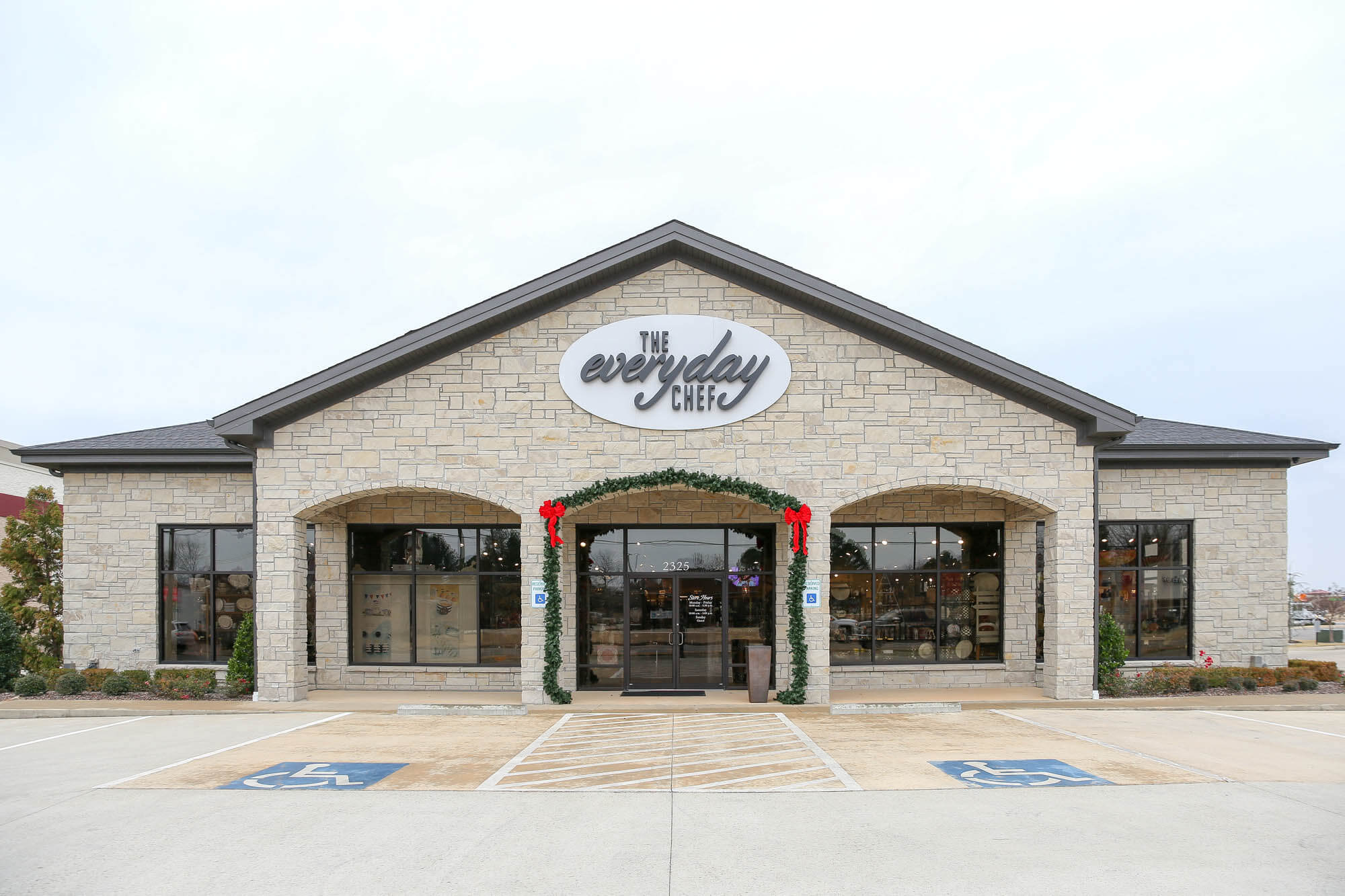 Straight-on exterior shot of 'The Everyday Chef' storefront, featuring a symmetrical design with a gabled roof, light-colored stone façade, and large arched entryway