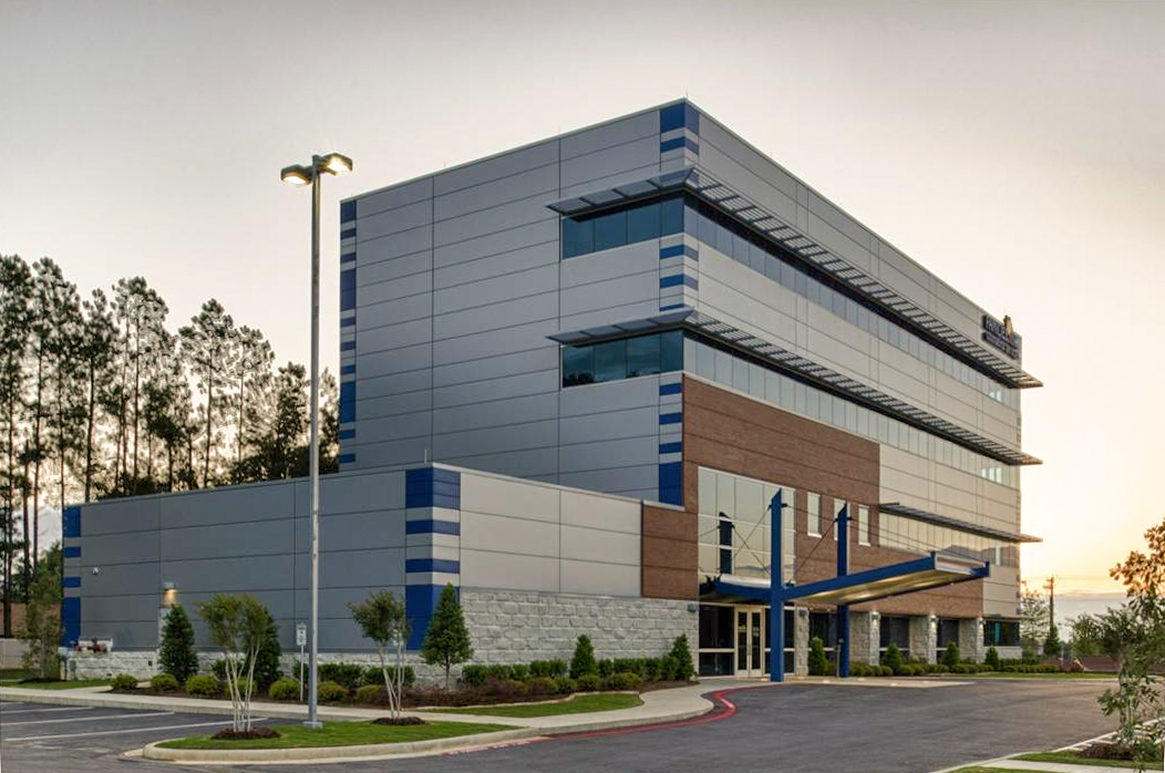 Four-story Families Inc. office facility with modern design, featuring horizontal metal panels, brick accents, large glass windows, and a covered entrance surrounded by landscaped grounds