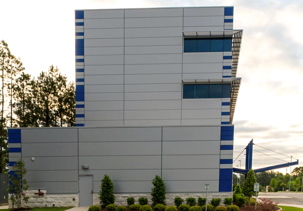Side view of Families Inc. office building with gray metal panels, blue striped accents, and two upper-level windows above landscaped greenery
