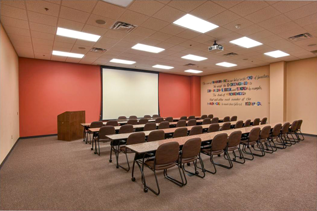 Families Inc. training and conference room with rows of tables, chairs, podium, projector, and large wall screen