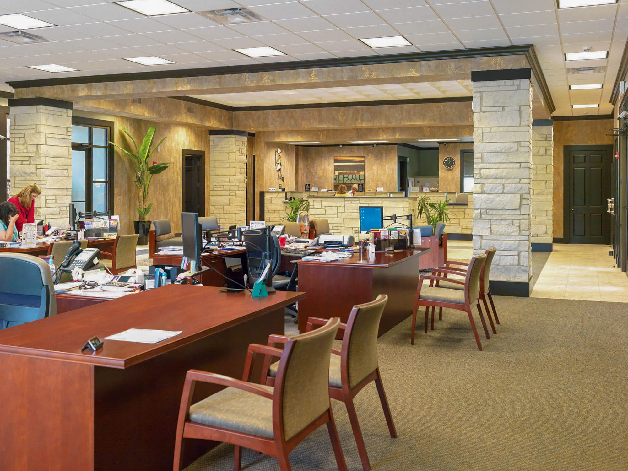 Interior shot of the main office area at Focus Bank, featuring an open-concept workspace with wooden desks, upholstered chairs, and computer stations