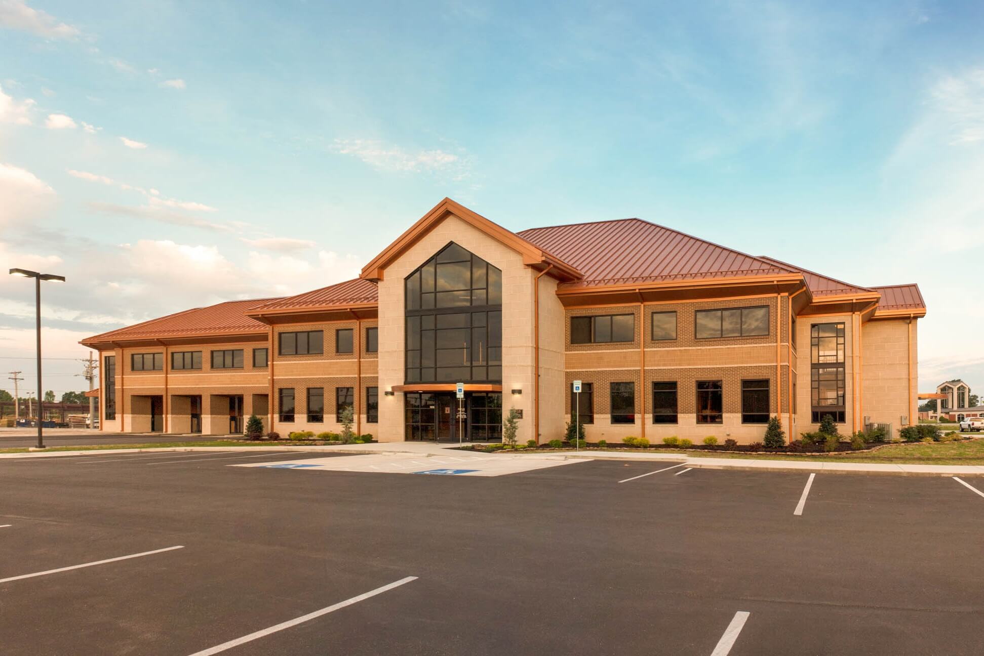 Straight-on exterior view of Focus Bank on Red Wolf Boulevard, featuring a two-story brick and stone building with a copper-toned roof, central glass entryway, and landscaped surroundings
