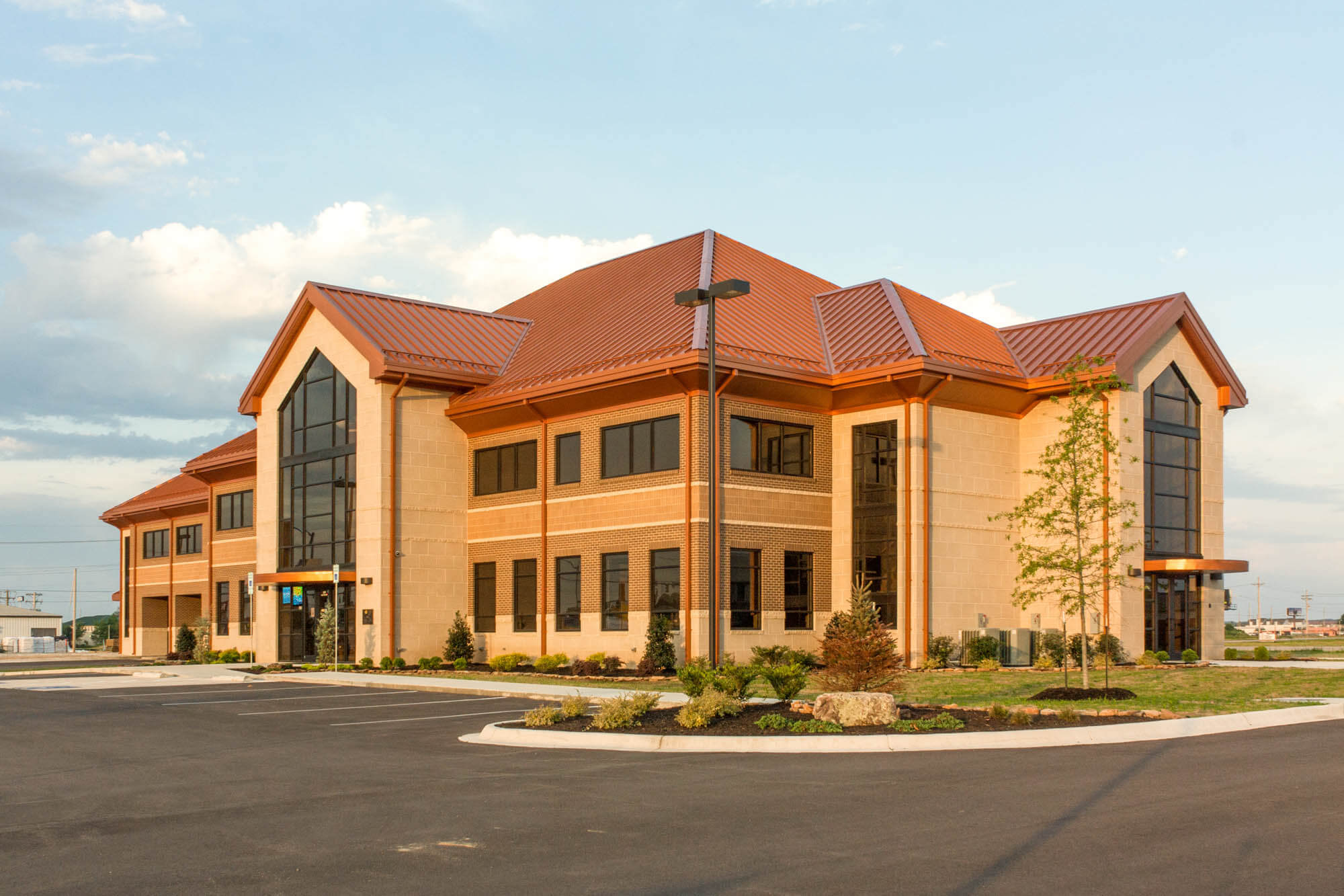 Angled exterior view of Focus Bank on Red Wolf Boulevard, featuring a two-story brick and stone building with a copper-toned roof, tall glass entryways, and landscaped grounds.