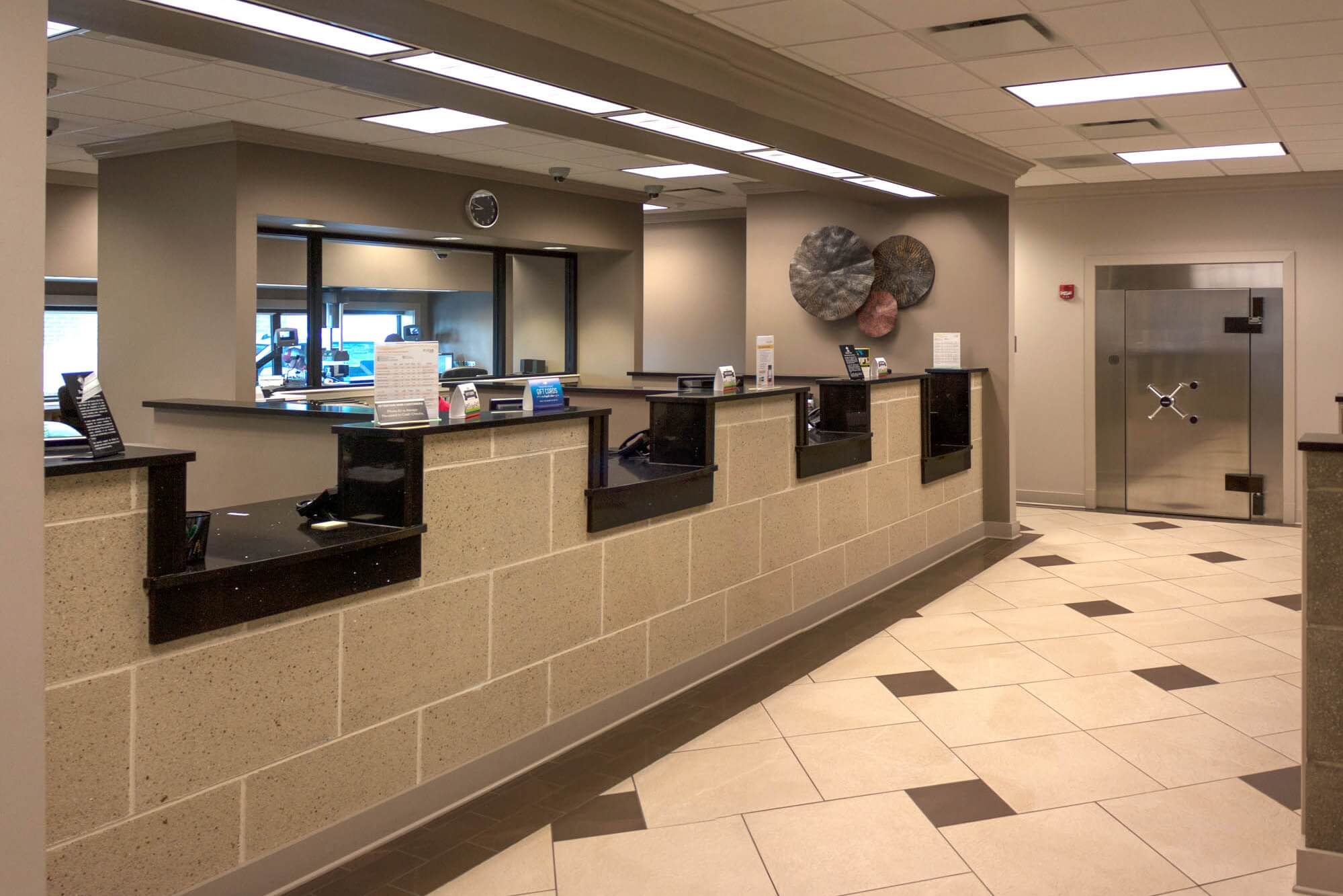 Interior view of the teller area at Focus Bank on Red Wolf Boulevard, featuring a stone-textured counter with multiple service windows, a decorative wall display, and a large vault door in the background