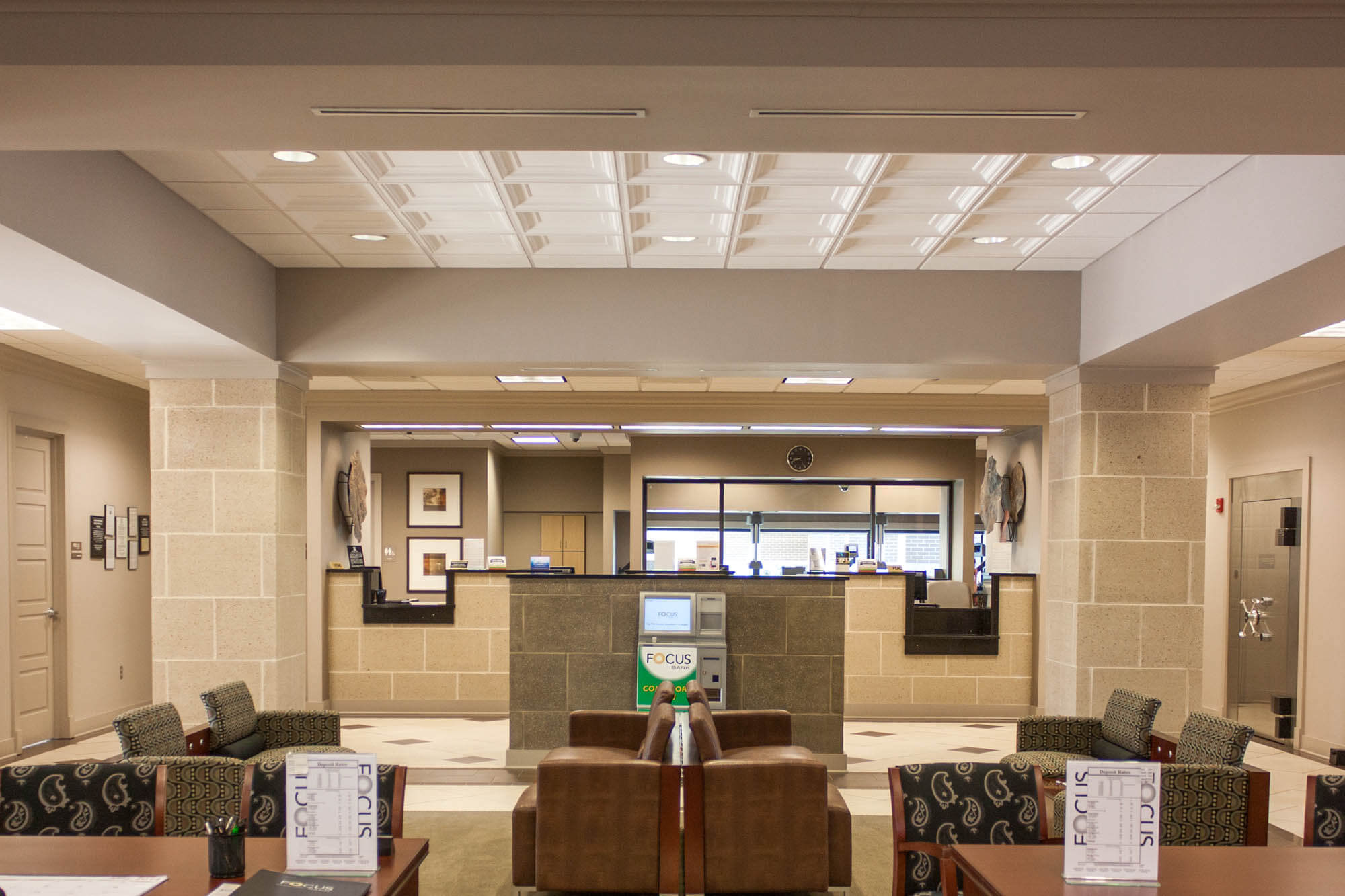 Interior view of the Focus Bank lobby on Red Wolf Boulevard, showing a seating area with leather and patterned chairs in the foreground and the teller counter with multiple service windows and a vault door in the background