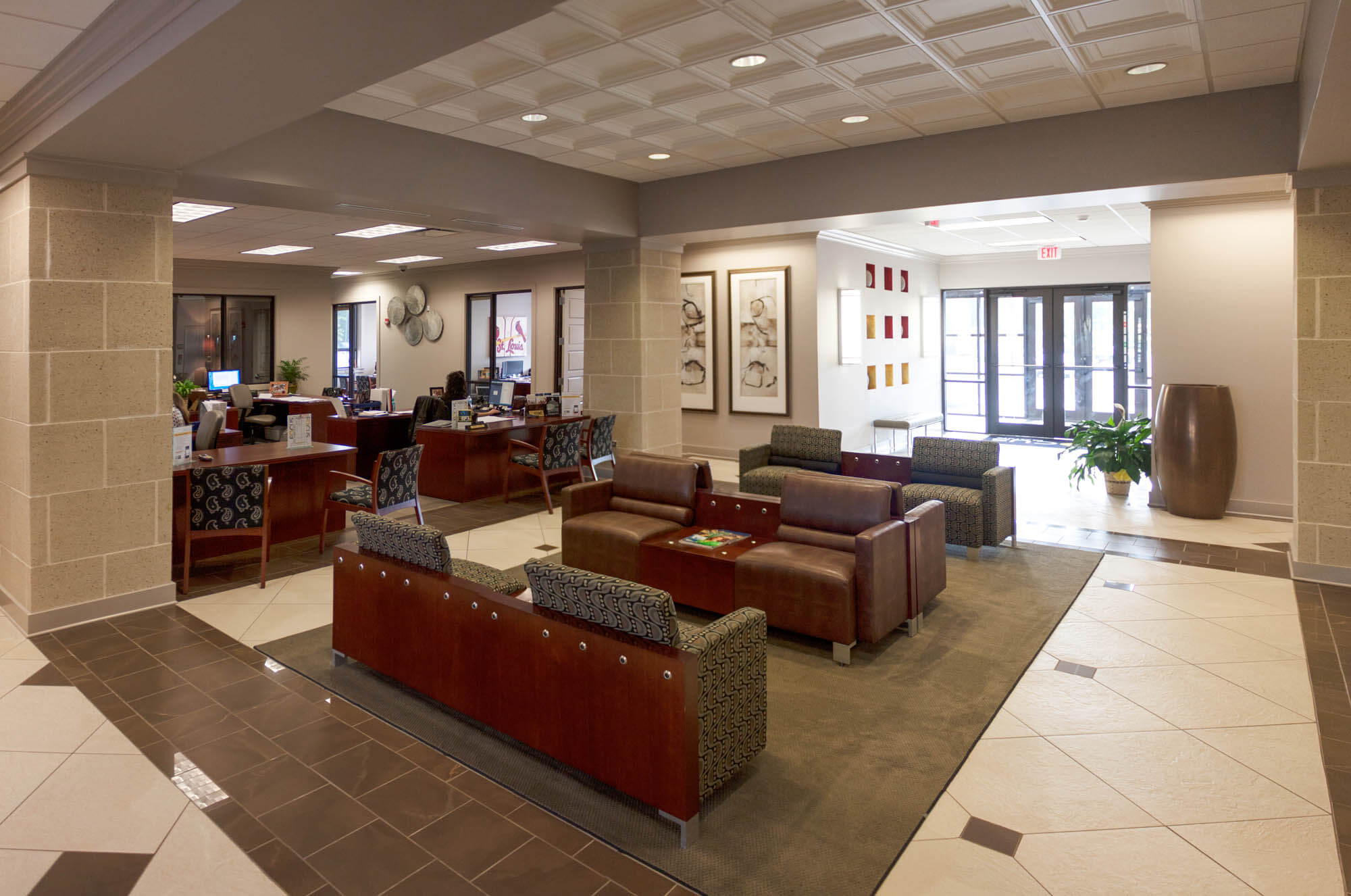 Interior view of the Focus Bank lobby on Red Wolf Boulevard, featuring a seating area with brown leather chairs and patterned armchairs in the center, individual desks for bank staff along the side, decorative wall art, and glass entry doors in the background
