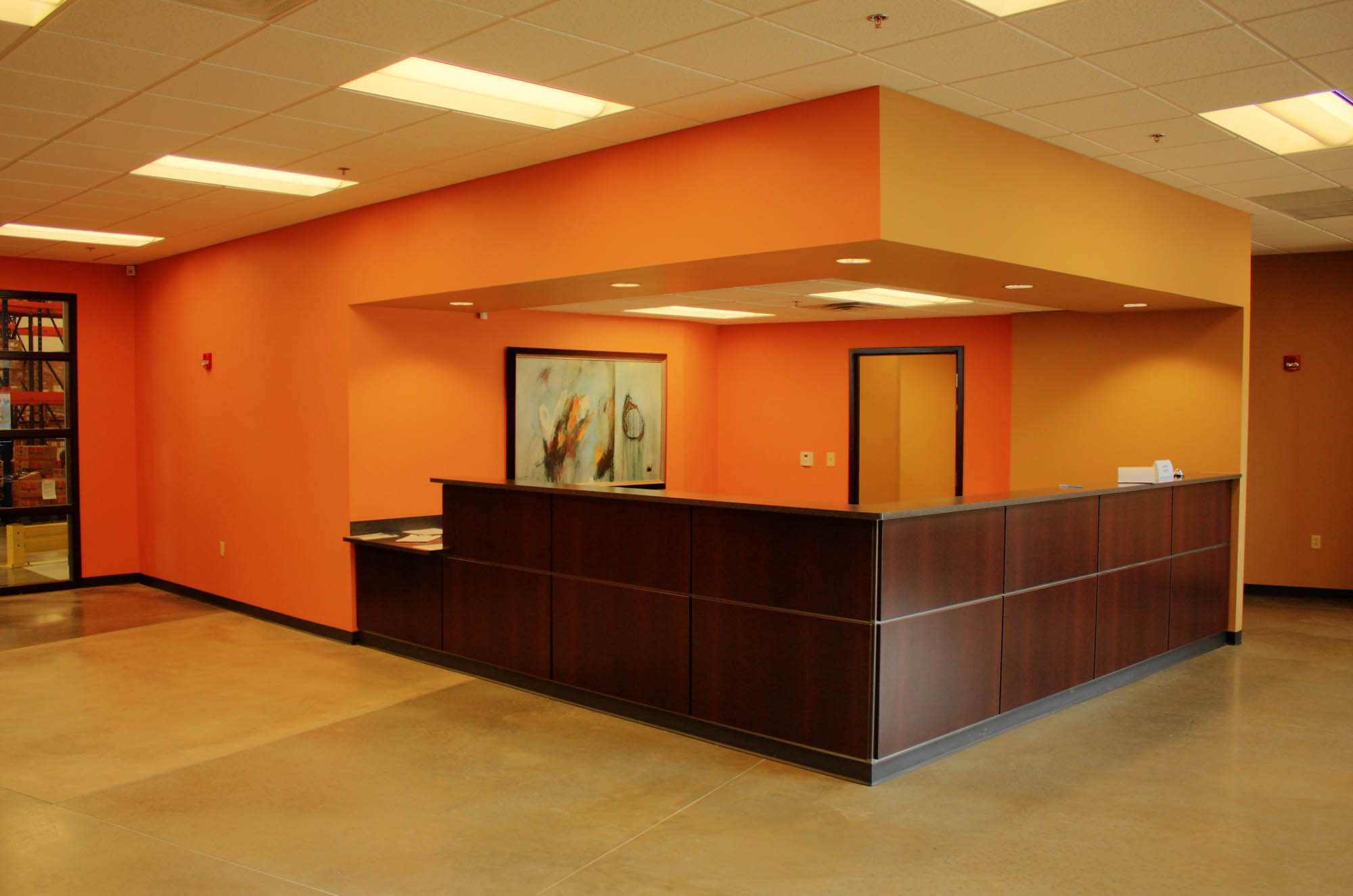 Interior shot of a reception area taken from a slightly angled perspective, highlighting a dark wood reception desk, polished concrete flooring, and vibrant orange walls
