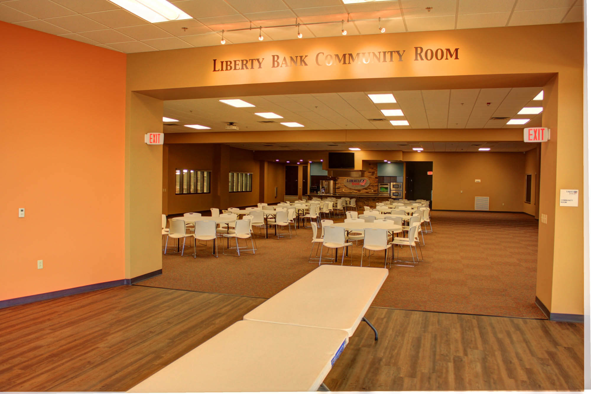 Interior shot of the Liberty Bank Community Room taken from a straight-on perspective, showcasing a warm colored, open event space with multiple round tables and white chairs