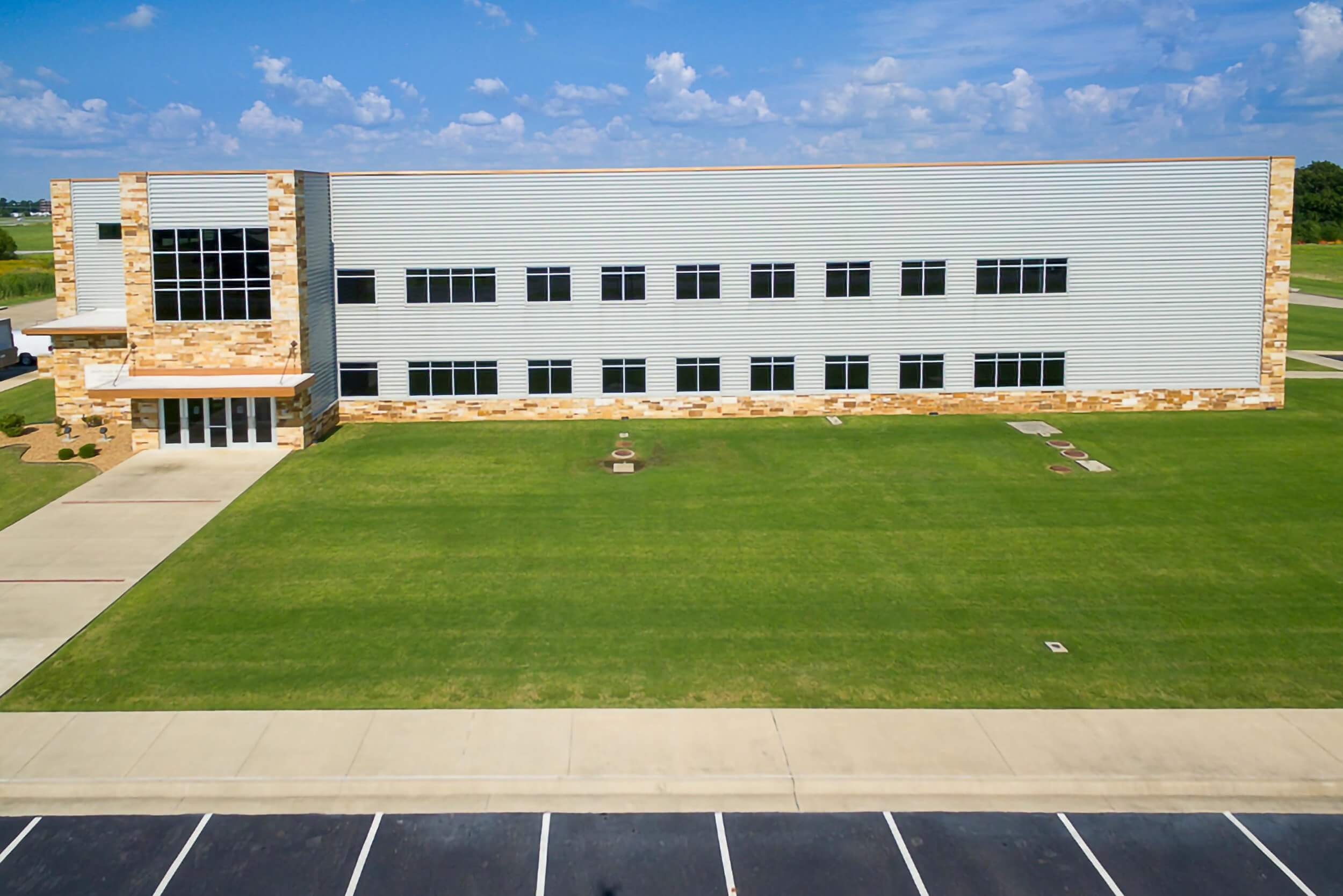 Elevated exterior drone shot a straight-on perspective. The façade features a mix of stone and metal siding, with large rectangular windows arranged symmetrically