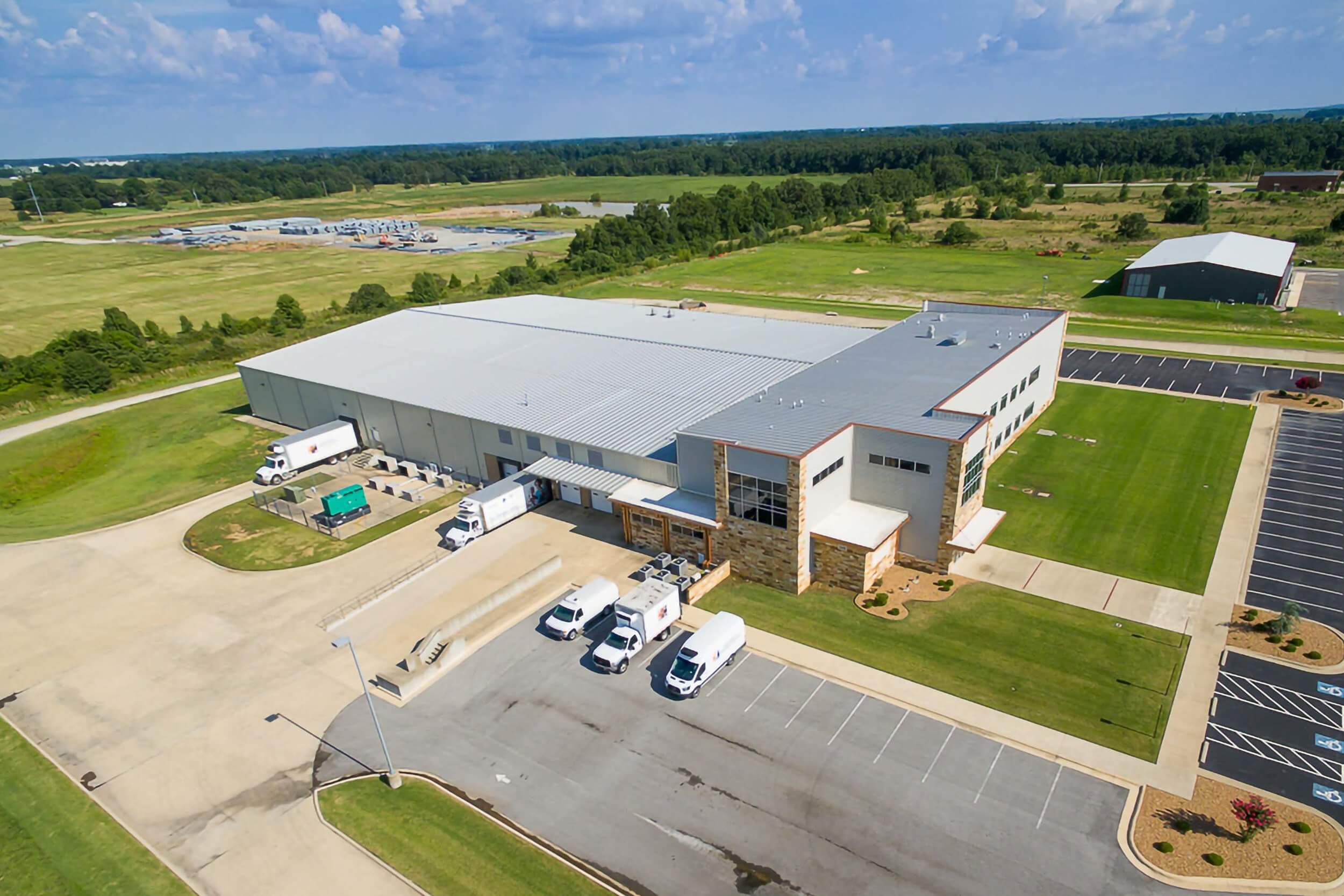 Exterior drone shot of the rear area includes multiple loading docks with trucks parked for deliveries, HVAC units, and a service entrance