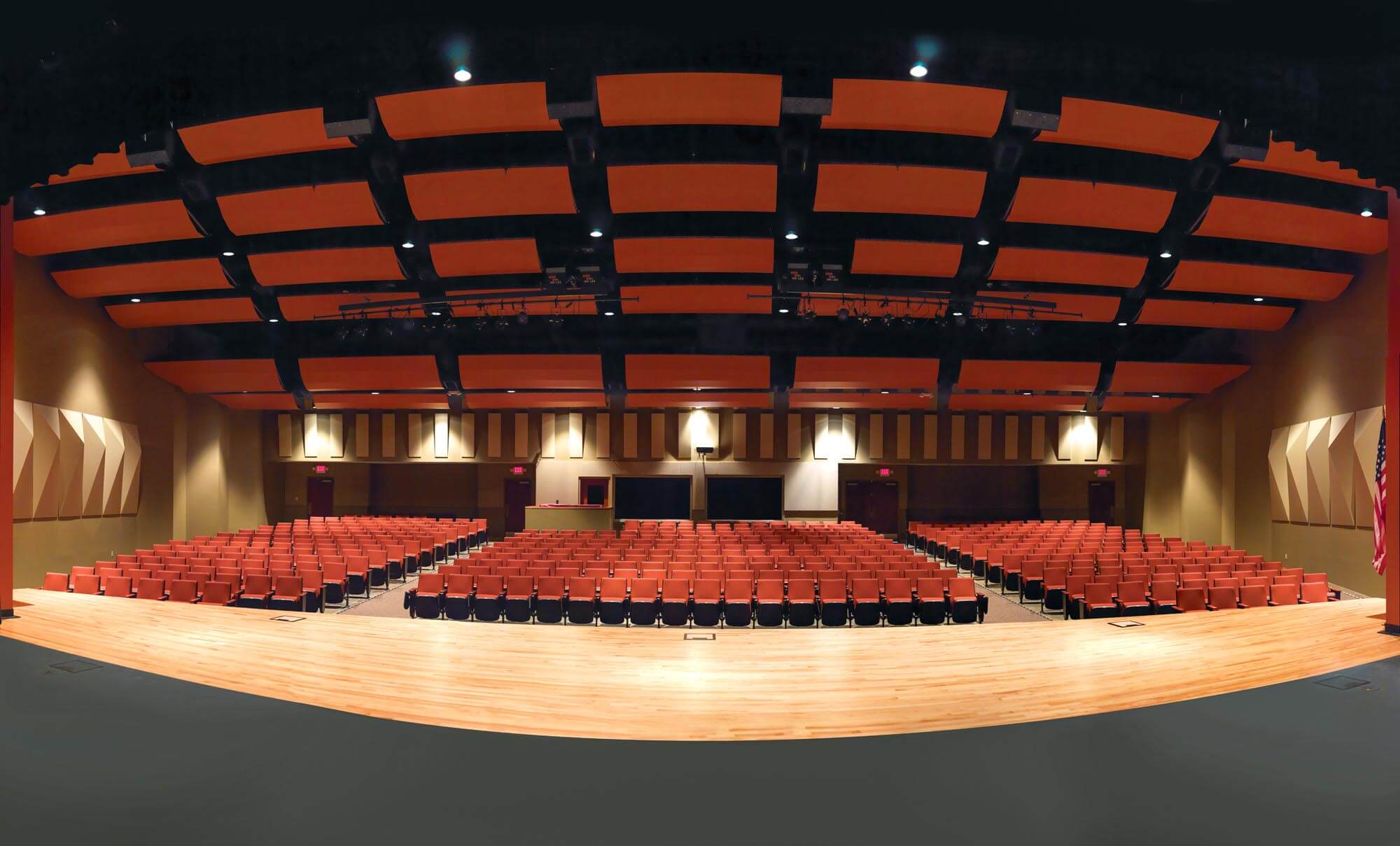 Interior of the performing arts auditorium with orange seats and suspended ceiling acoustic panels, view from the stage area