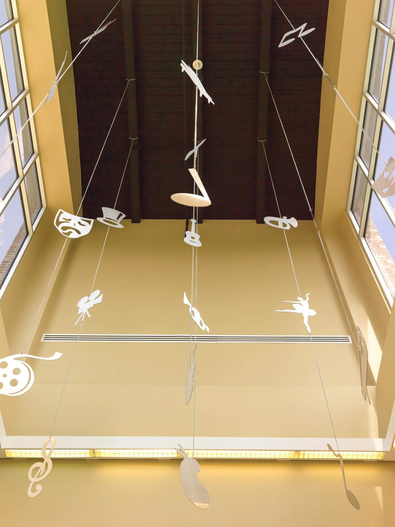 Atrium decorated with suspended white mobiles representing various arts, tall windows and high ceiling