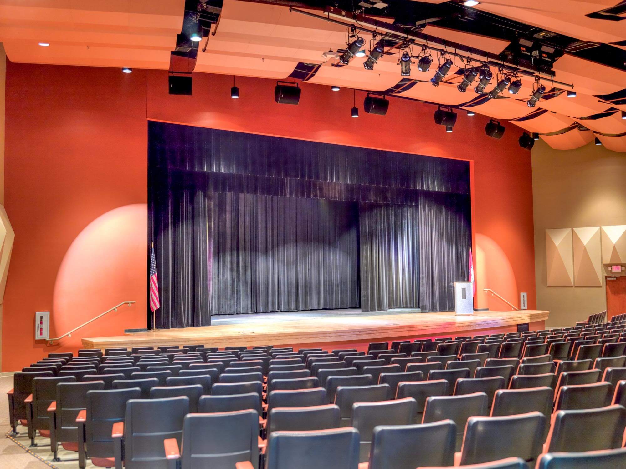 Auditorium viewed from the seating area showing the stage, black curtain, orange acoustic panels and stage lighting