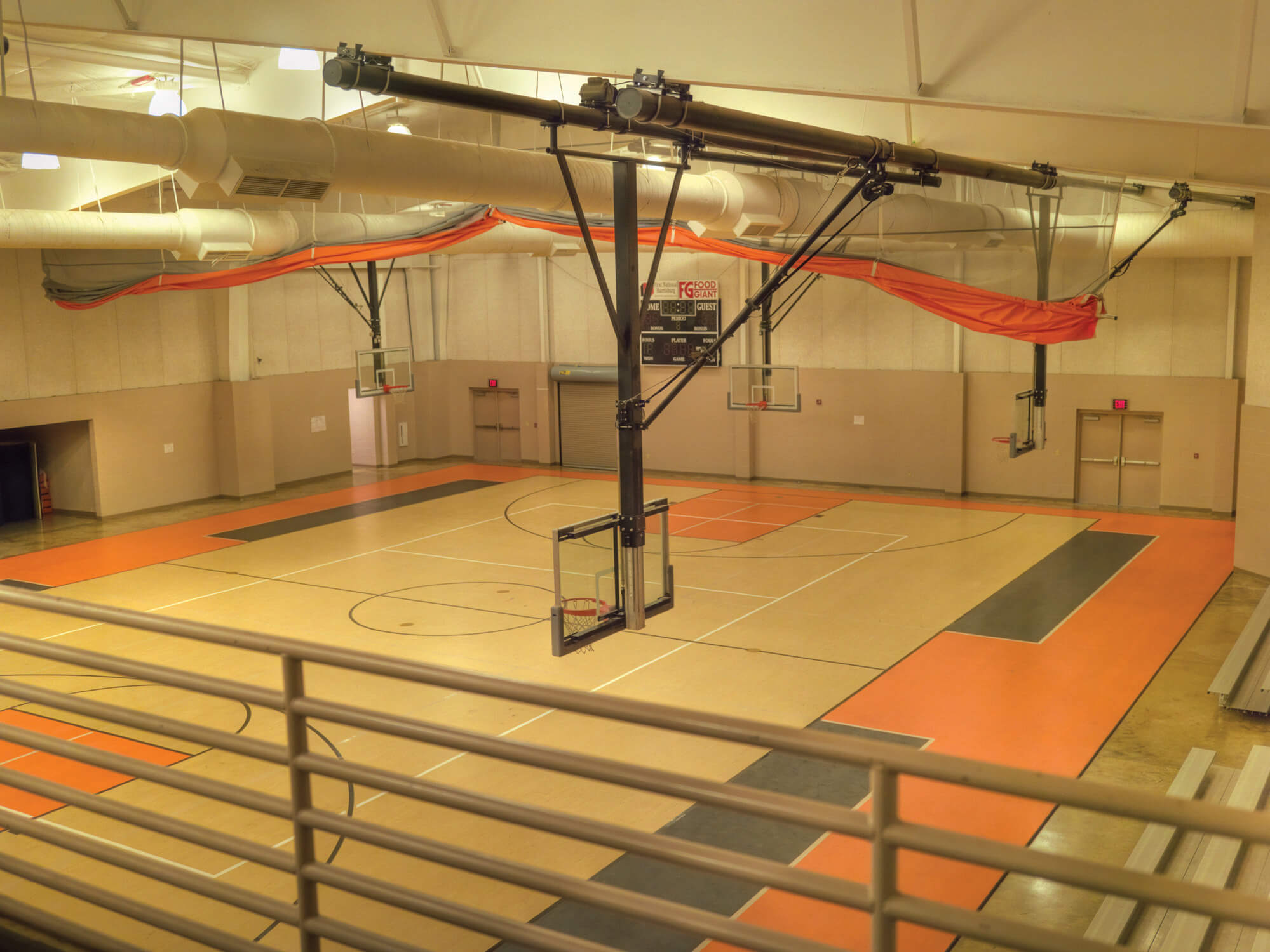 Interior gymnasium with multi-colored sports floor, basketball goals and exposed mechanical ducts