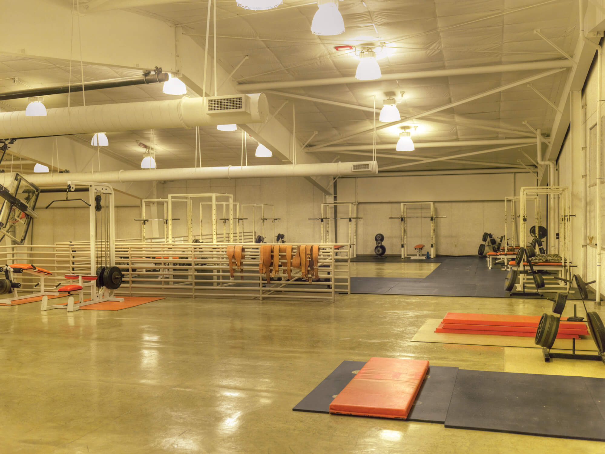 Weight-training area containing equipment racks, benches and exposed truss ceiling