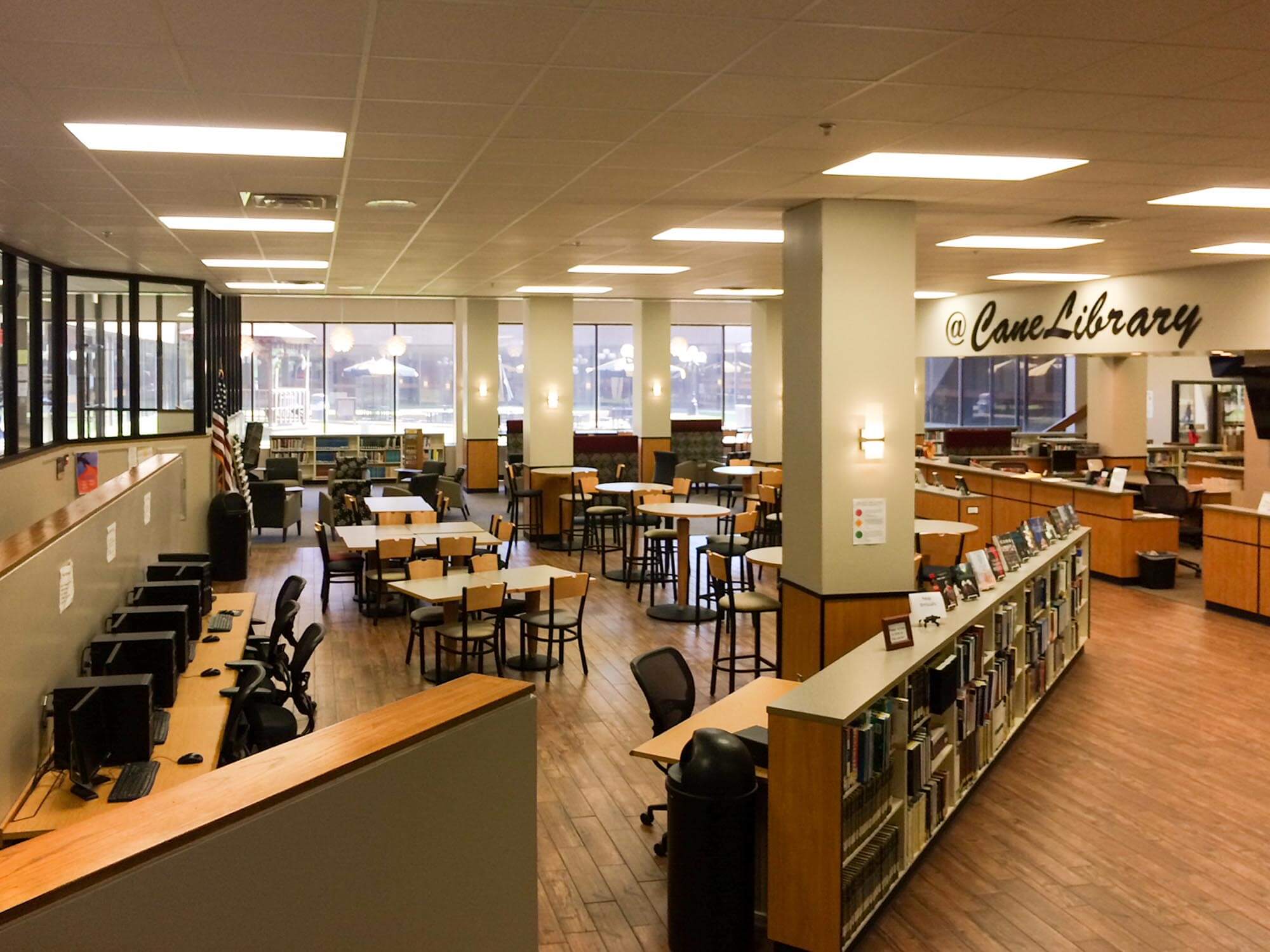 Open interior showing computer workstations, collaborative tables, book displays and “@ Cane Library” sign