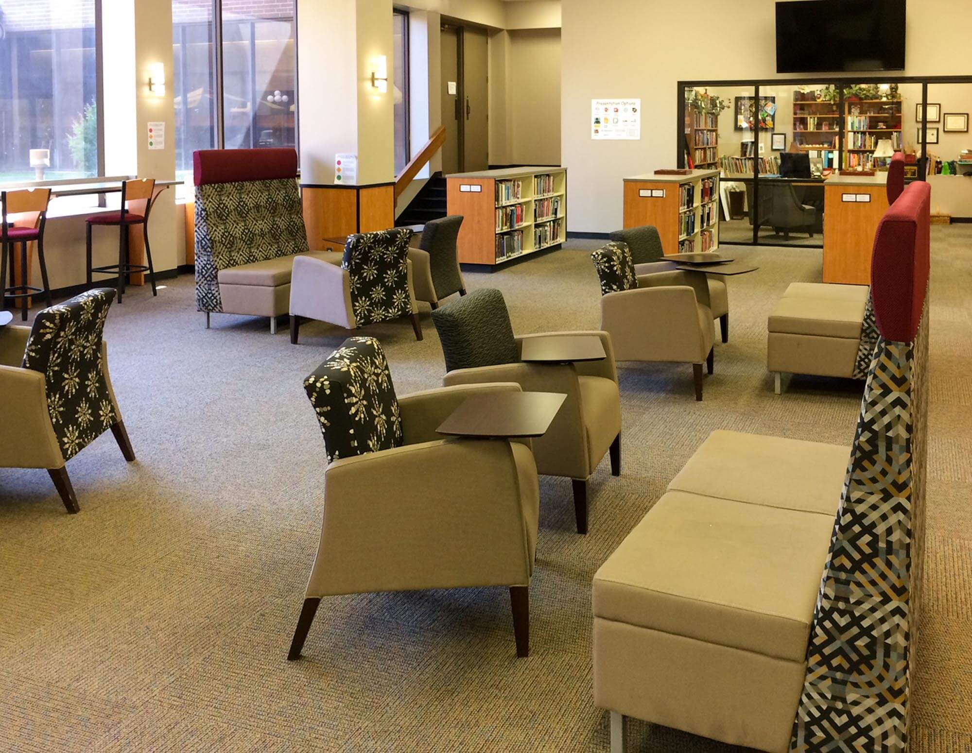 Seating area with varied chairs, cushioned benches, built-in bookcases and large windows letting in natural light
