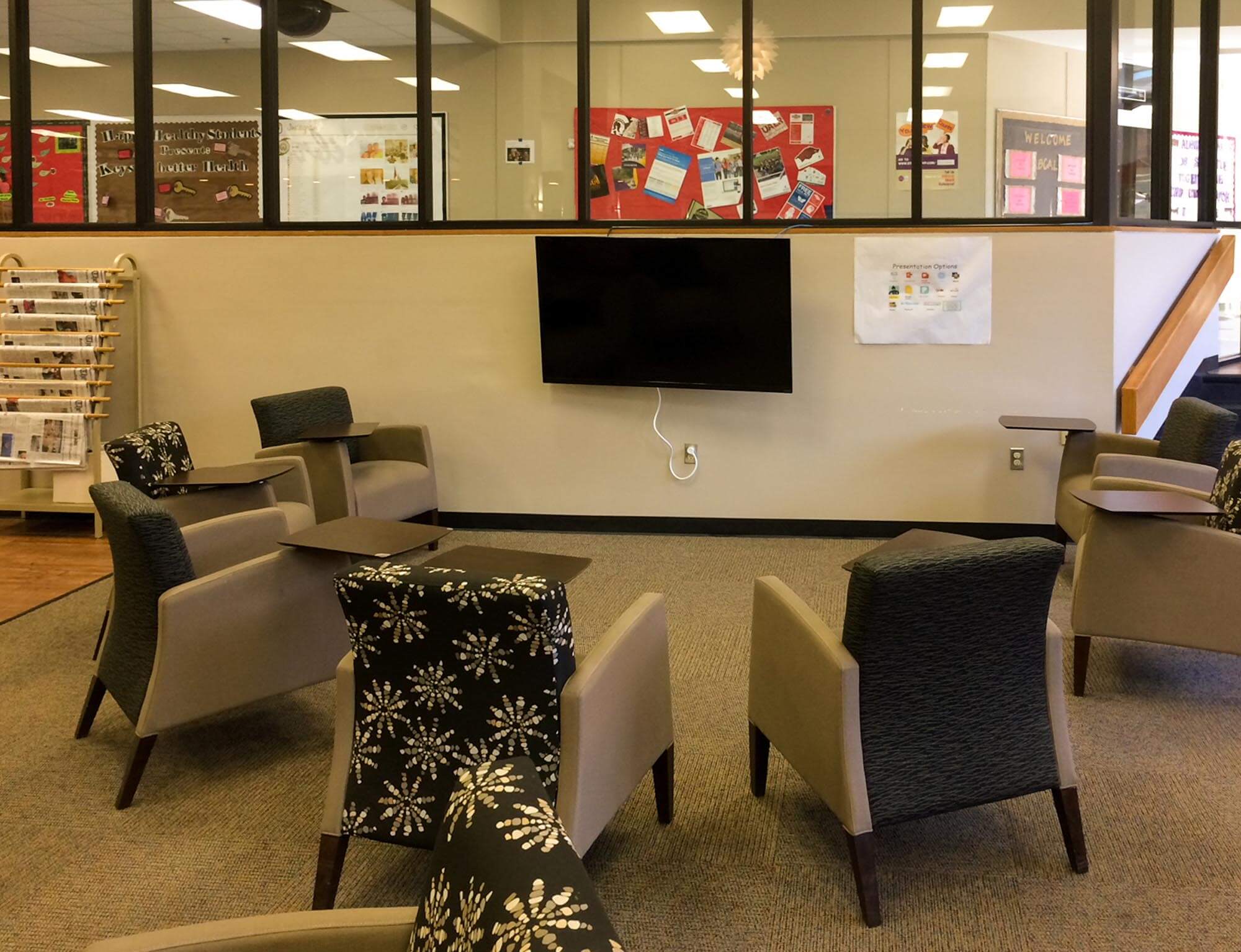 Group collaboration area featuring chairs around a wall-mounted screen and glass partition