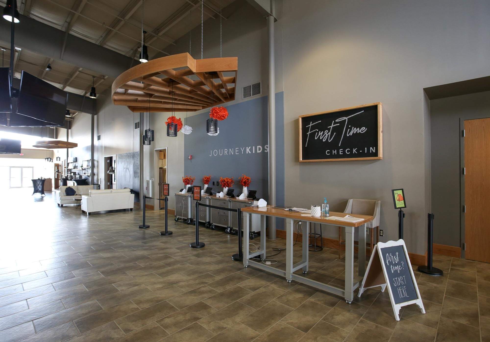Journey Baptist Church lobby with First Time Check-In desk, JOURNEYKIDS wall sign, hanging wood fixtures, and seating area