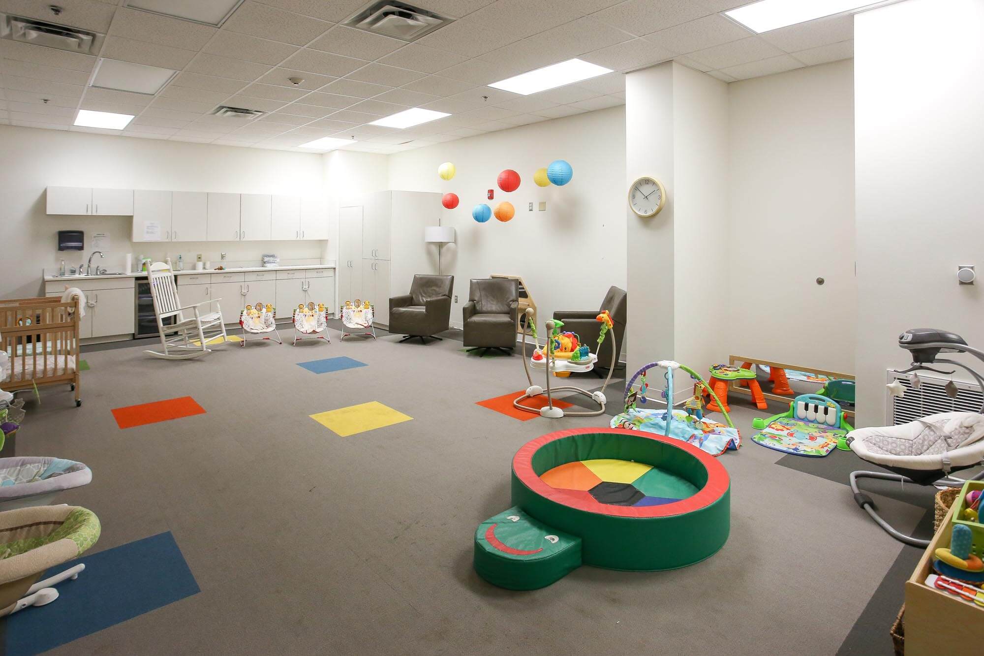 Journey Baptist Church nursery with cribs, rocking chair, colorful hanging lanterns, leather chairs, play mats, toys, baby swings, and cabinets along the back wall