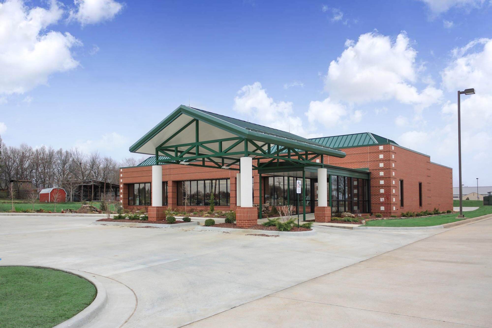 Exterior of the brick clinic with teal metal roof and green steel canopy over the entrance, set beside a large parking lot