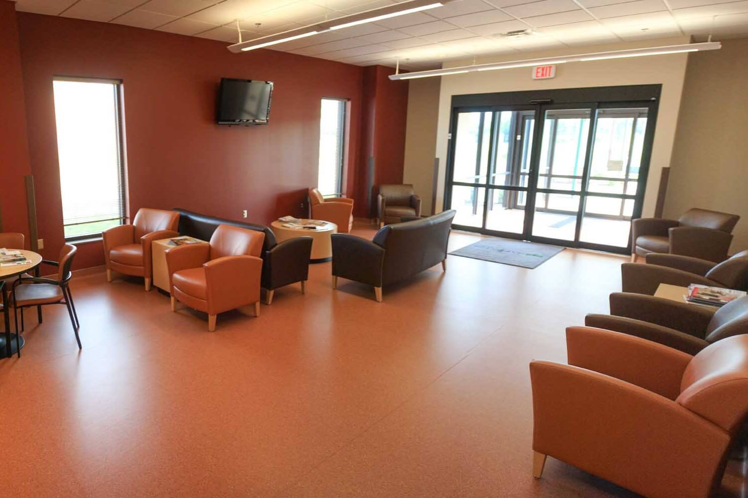 Interior waiting area furnished with lounge chairs, red accent wall, television and glass entrance