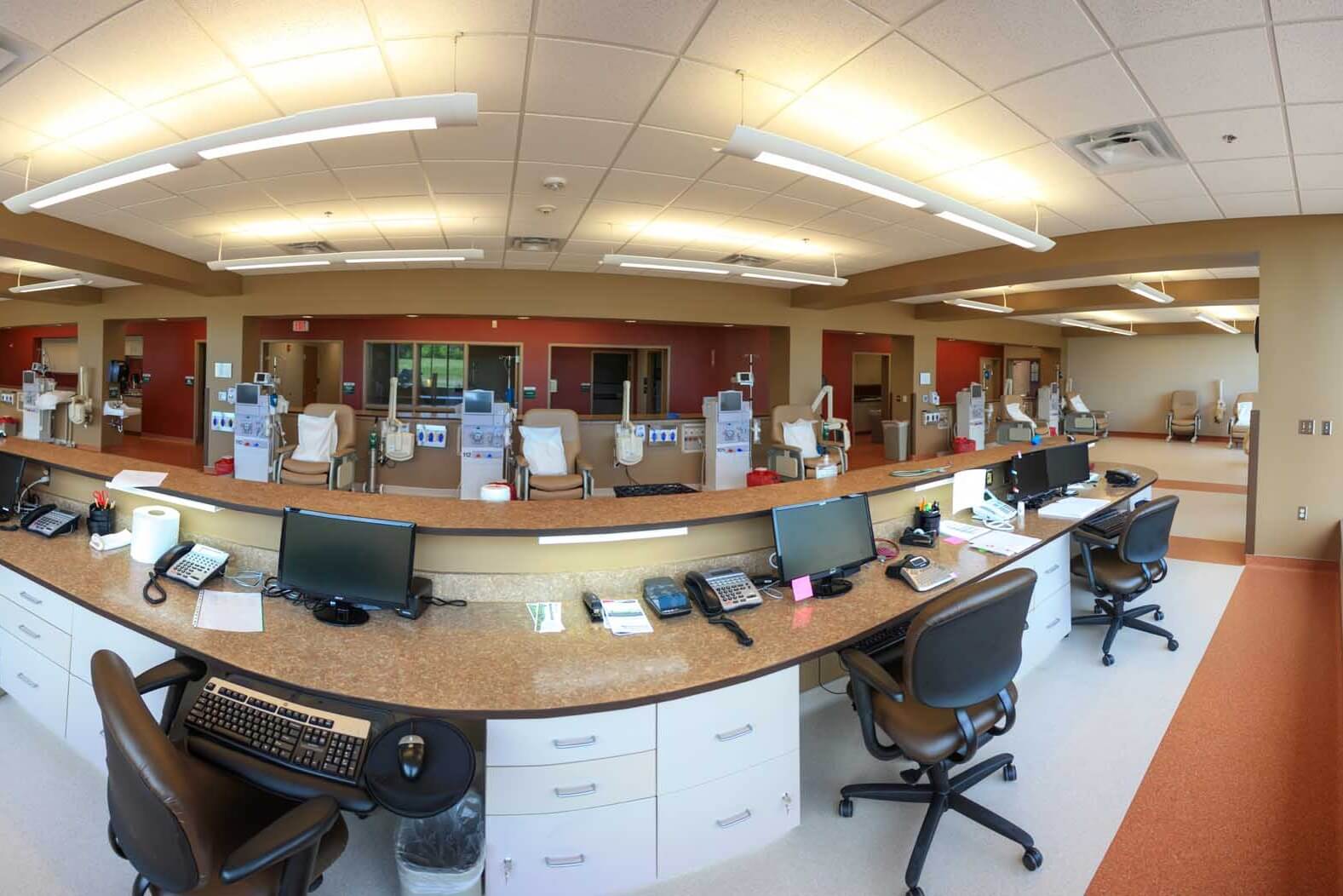 Dialysis treatment room with a central nurse station surrounded by multiple dialysis machines and chairs