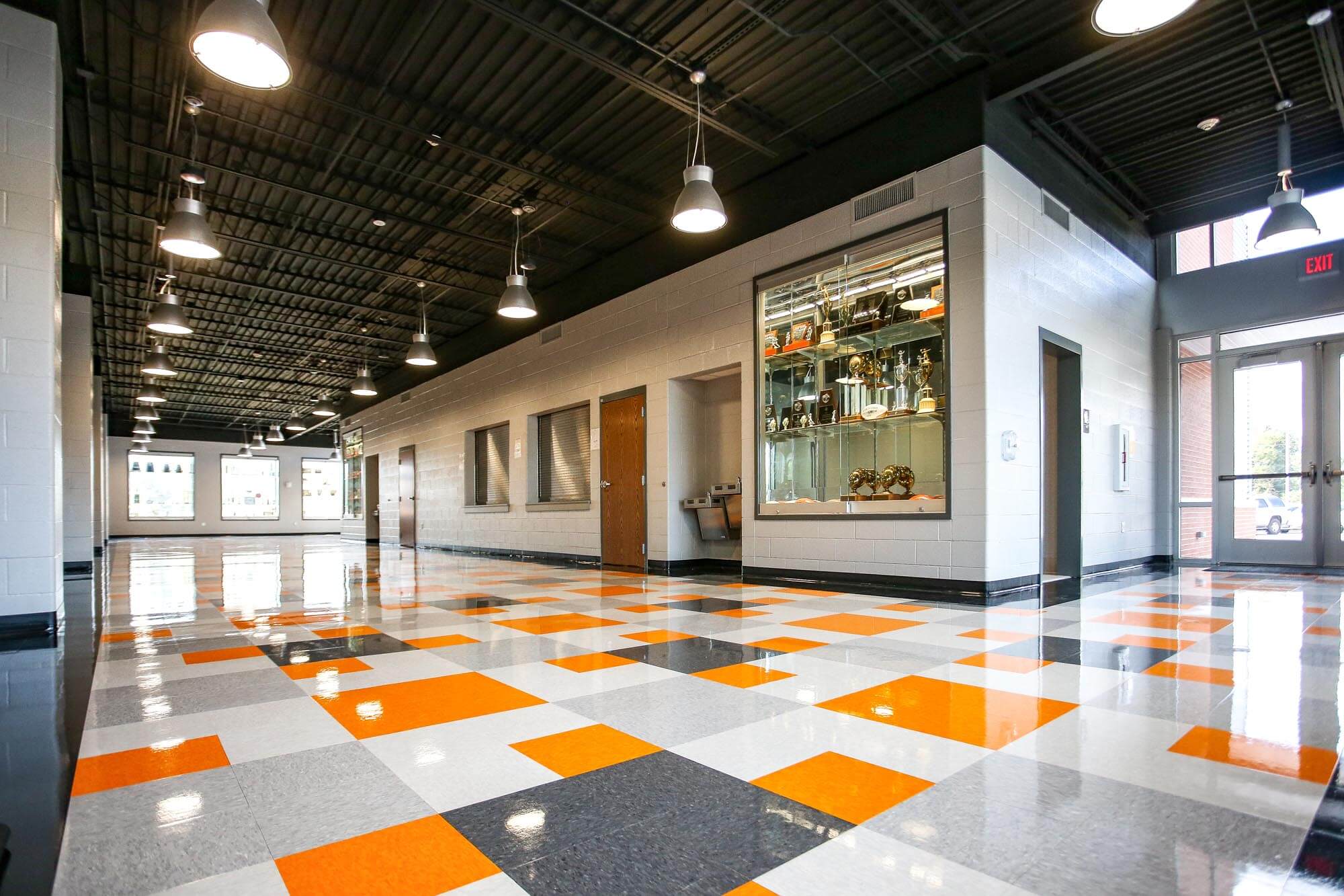 Lobby view highlighting the vibrant checkerboard floor, glass trophy display and industrial pendant lights