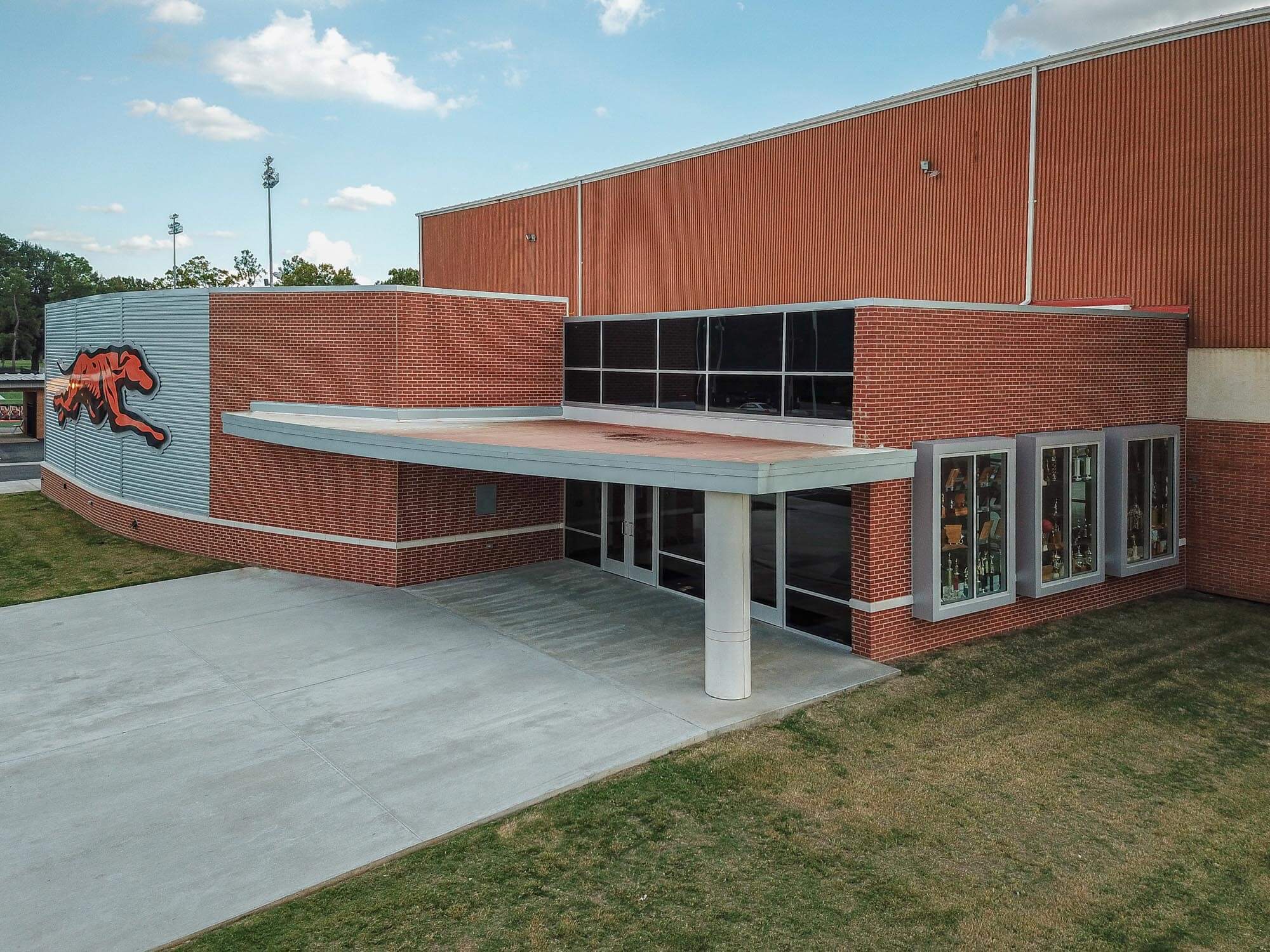 Angled aerial view revealing the curved brick front, glass trophy room and cantilevered canopy supported by a large column