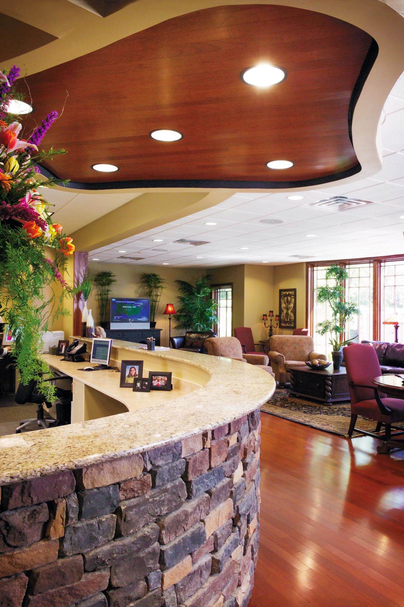 Reception area of Parkey-Davis Dental Clinic with curved stone-front desk, granite countertop, warm wood floors, and comfortable seating in a spacious, well-lit waiting area