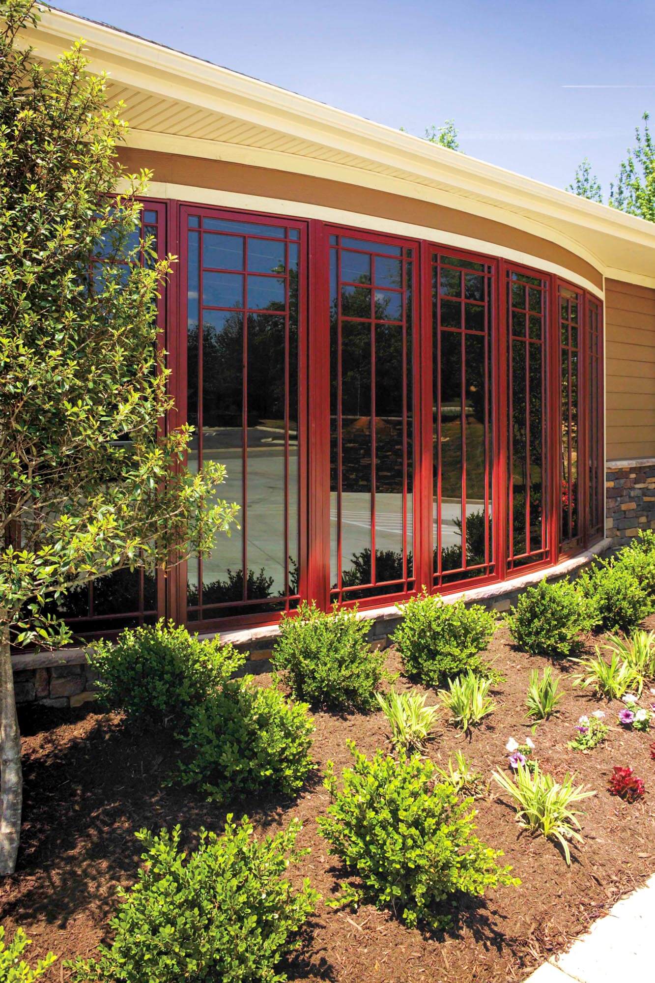 Exterior view of Parkey-Davis Dental Clinic’s curved bay windows with red trim, surrounded by landscaped shrubs and plants