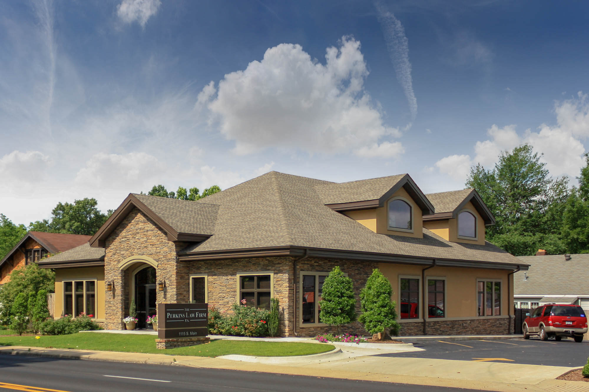 Evening exterior of the Perkins Law Firm building showing a multi-gabled roof with stone and stucco façade, an arched entry porch, manicured landscaping and parking lot