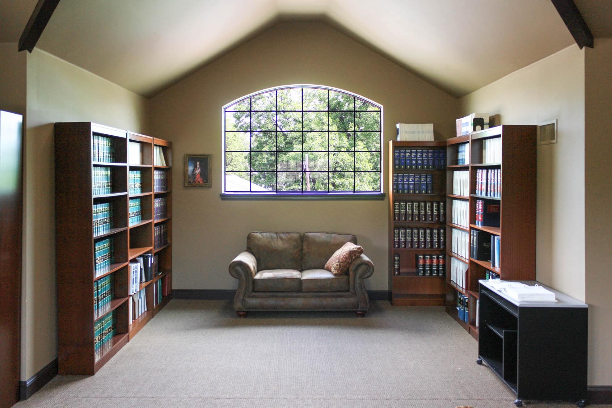Library/waiting room featuring wooden bookcases filled with legal volumes, an arched window, tufted sofa and accent table