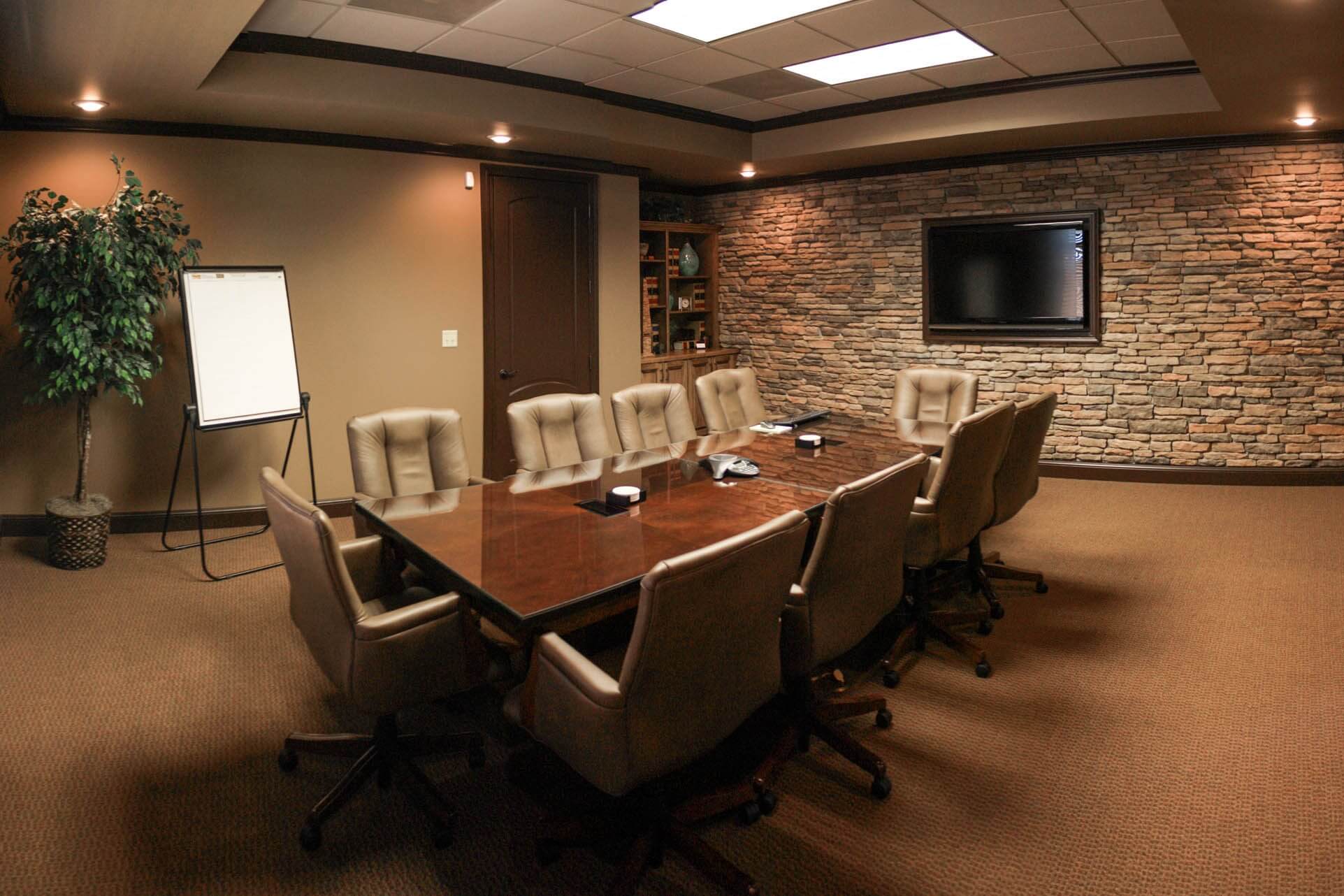 Large conference room with long wooden table, beige leather chairs, stone feature wall with television and a whiteboard
