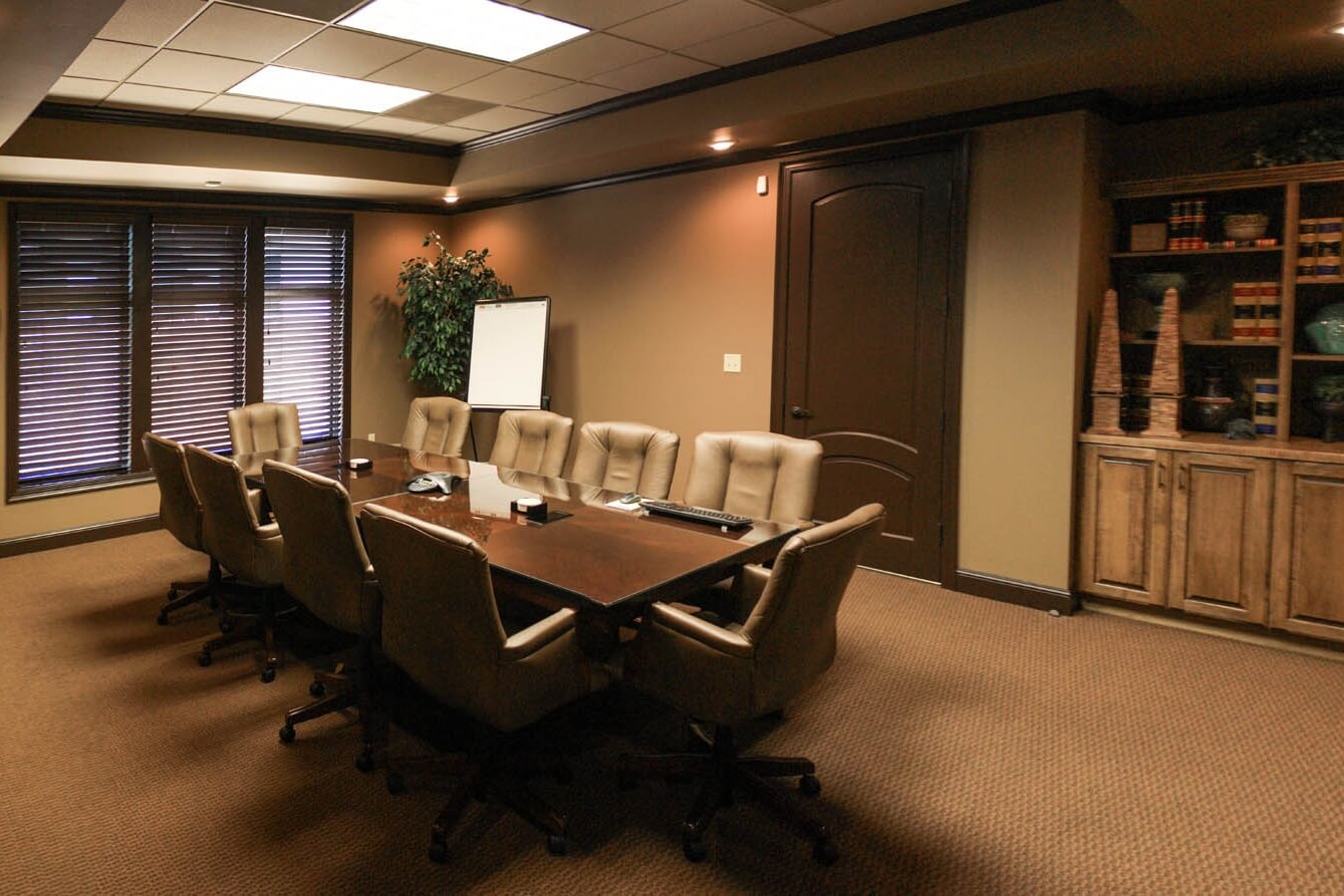 View of conference room showing wood table and beige chairs, built-in wood cabinets, door and window with blinds