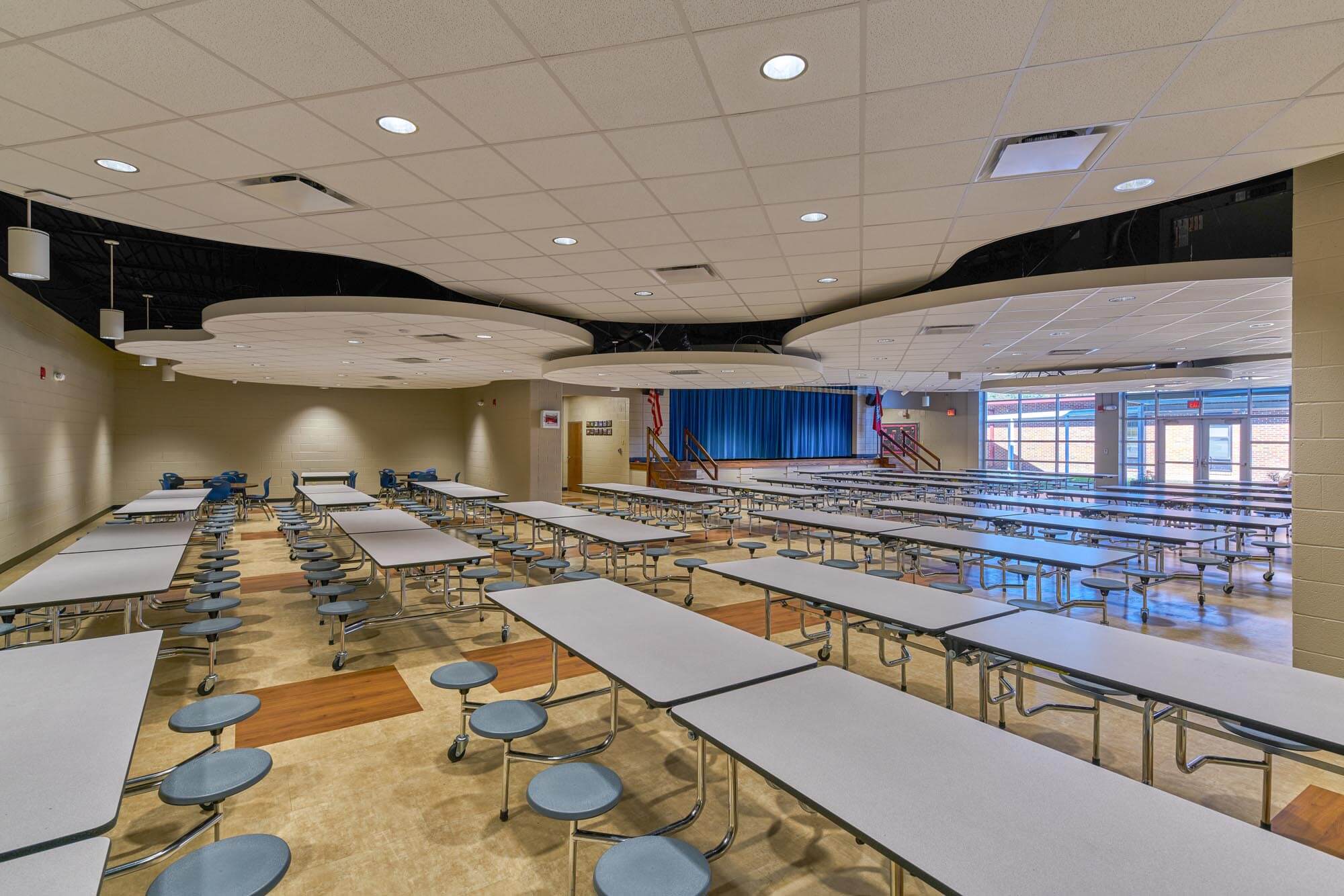 Richland Elementary cafeteria with long tables, circular light features, and stage with blue curtain