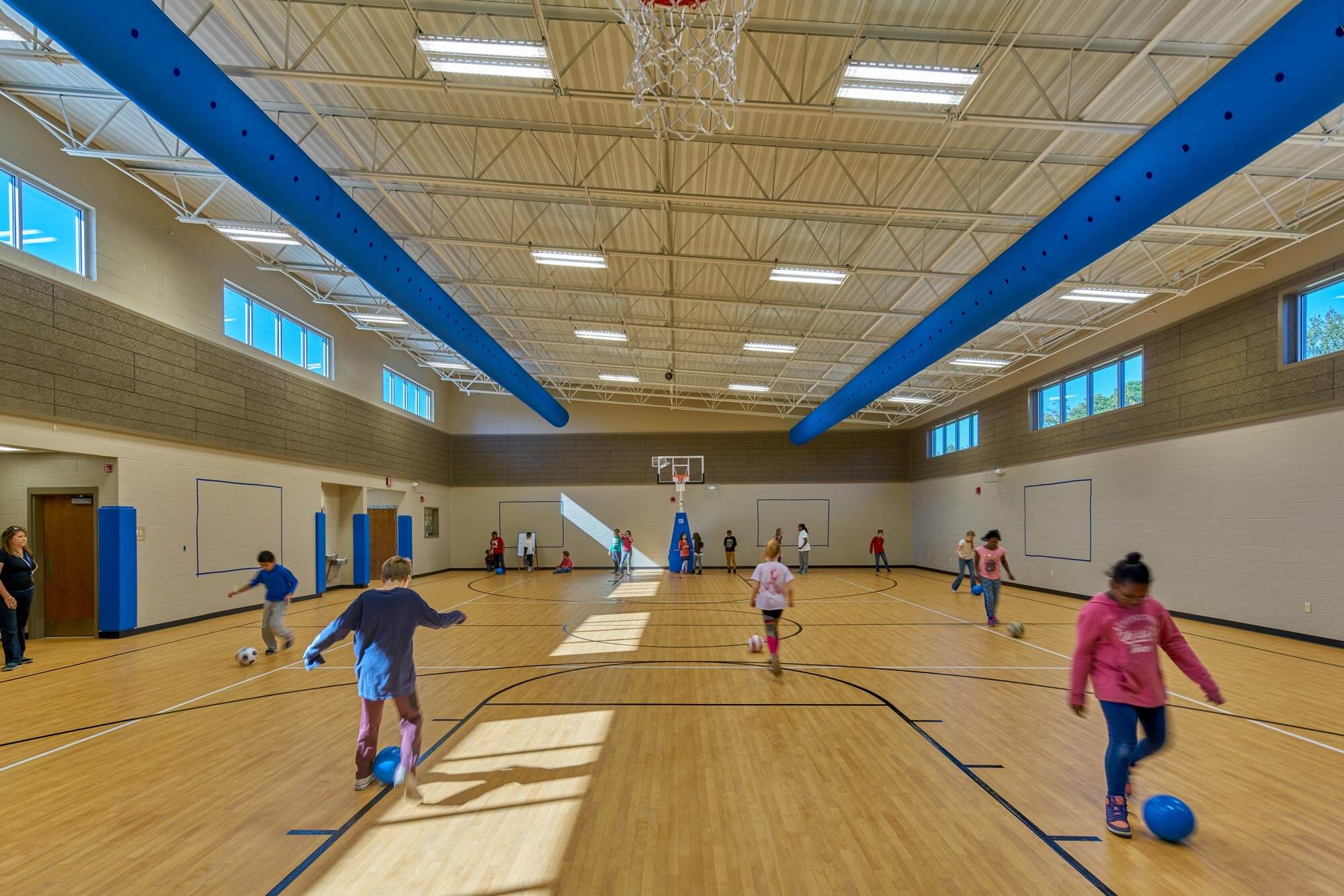 Children playing soccer and basketball in Richland Elementary gym with natural light from high windows