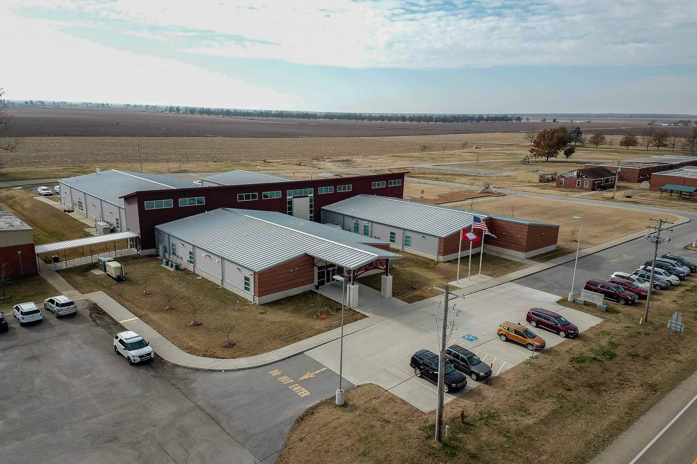 From angle, aerial view of the campus showing multiple buildings connected by covered walkways with farmland in the background