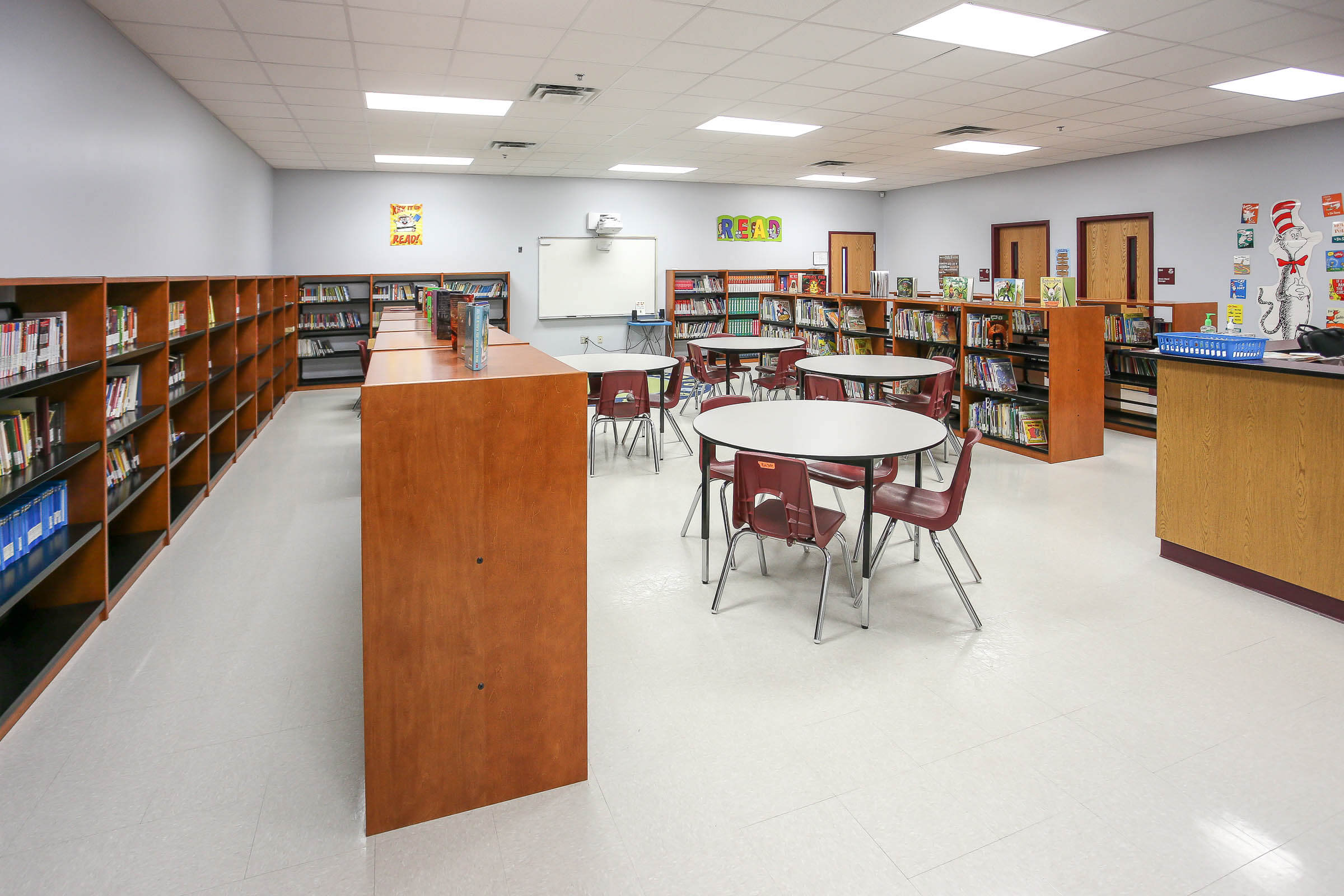 Library interior featuring bookshelves, round tables, grey tile floor and walls decorated with posters