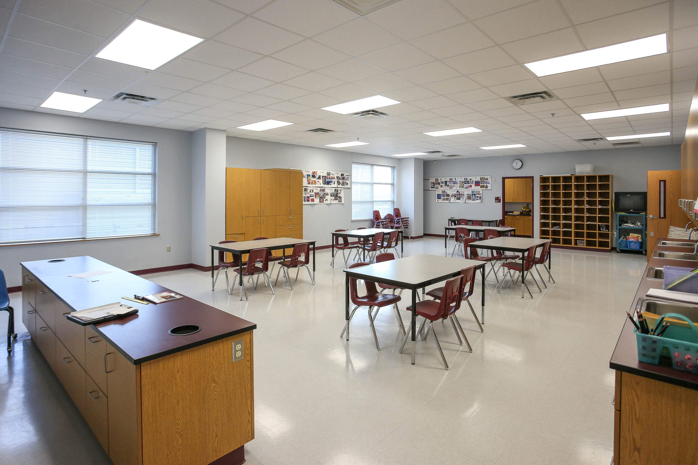 Multi-purpose classroom outfitted with tables, chairs, built-in cabinets and sink along the wall