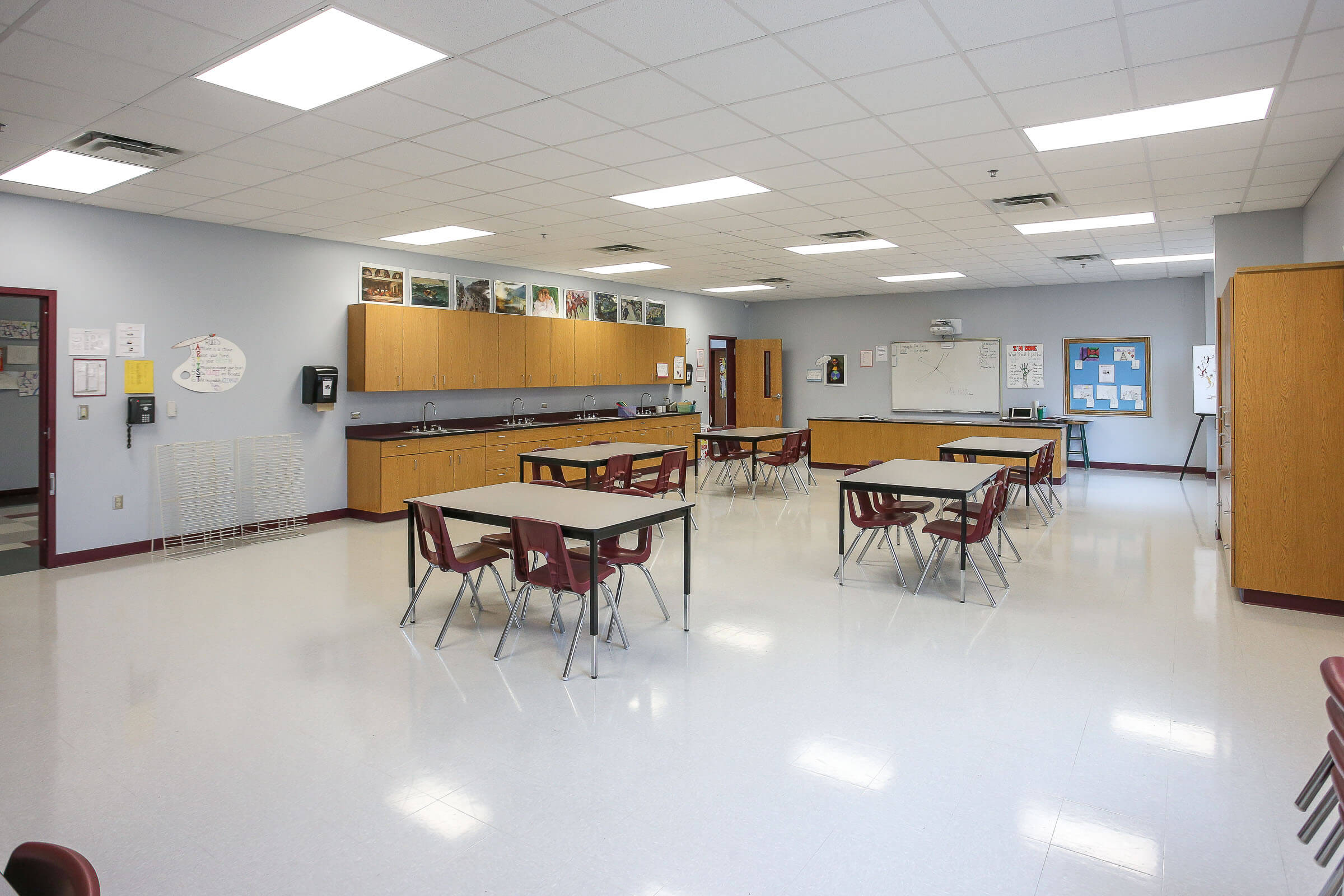 Multi-purpose classroom outfitted with tables, chairs, built-in cabinets and sink along the wall