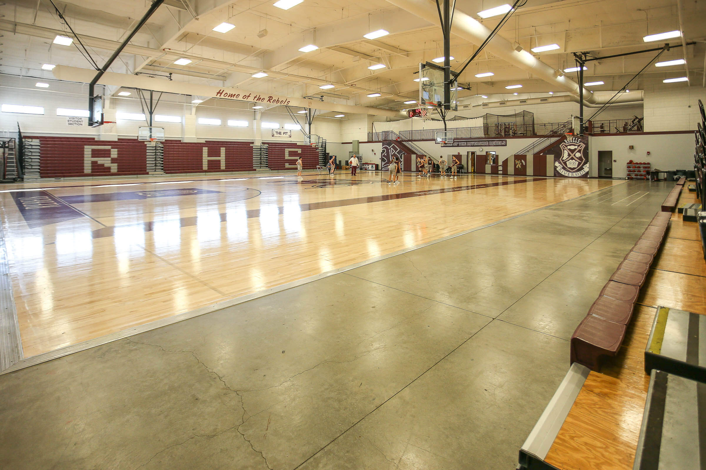 Wide angle of the gym showing bleachers and players practicing on the polished court
